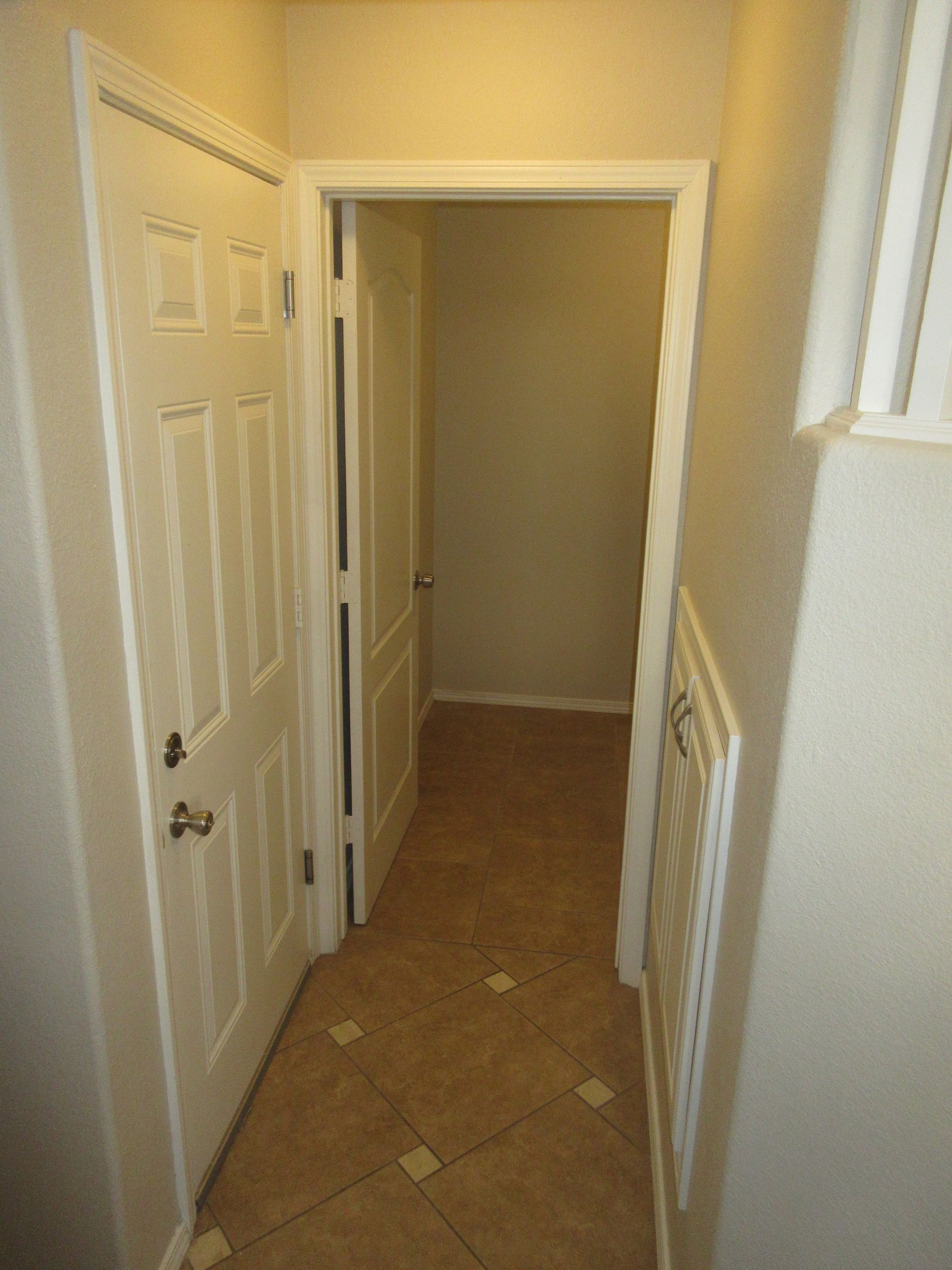 A hallway with a door that is open and a tiled floor.