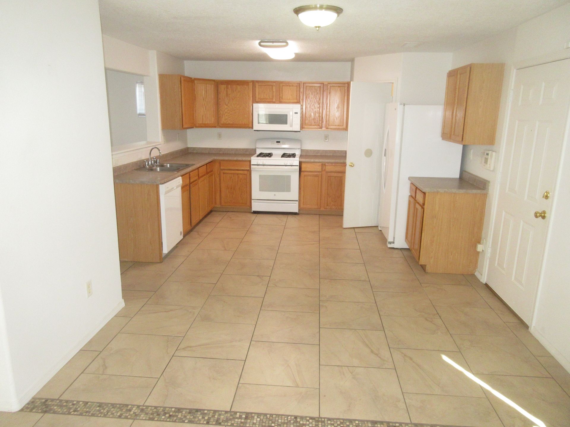 An empty kitchen with wooden cabinets and white appliances
