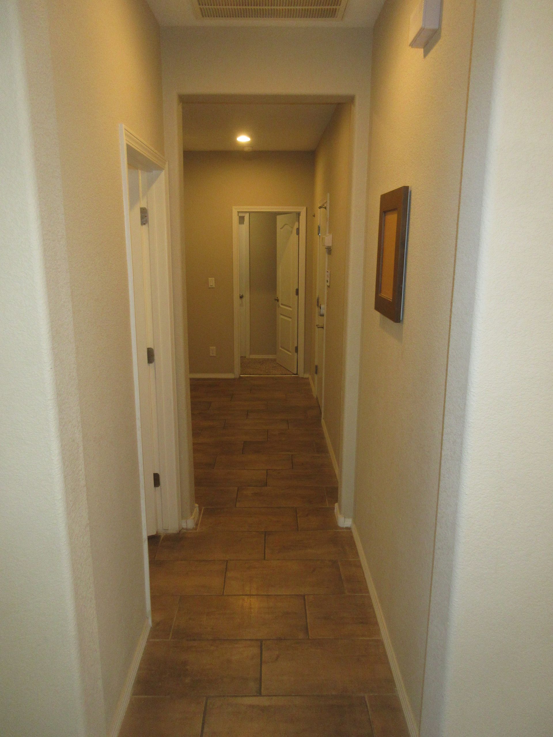 A long hallway with a tiled floor and a picture on the wall.