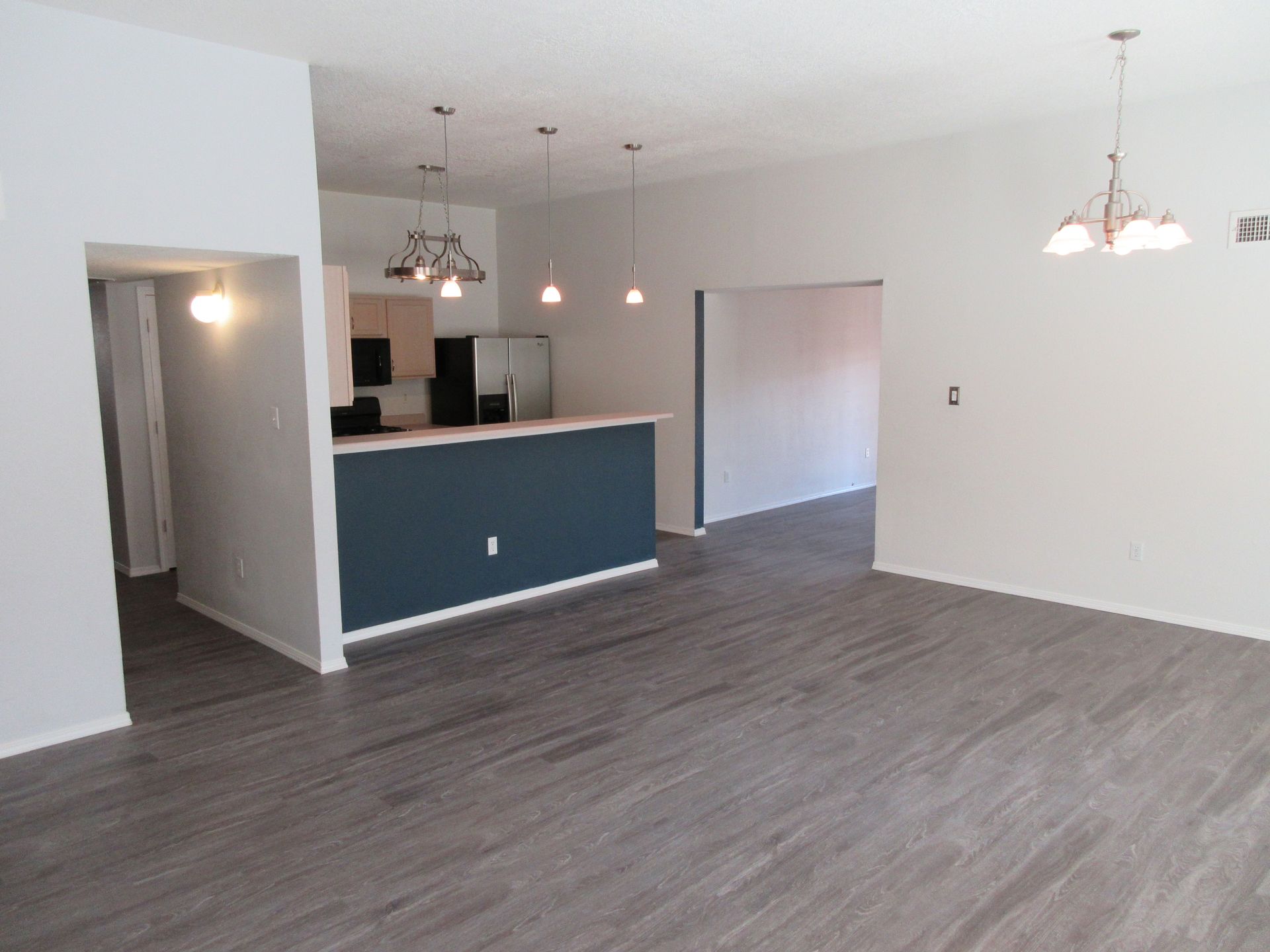 A living room with hardwood floors and a kitchen in the background.