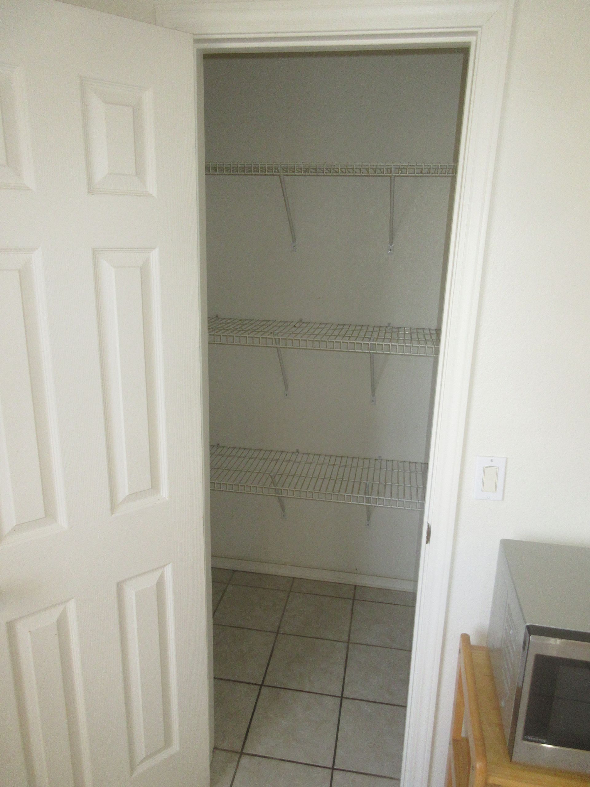 A white door is open to a closet with a microwave in the corner.