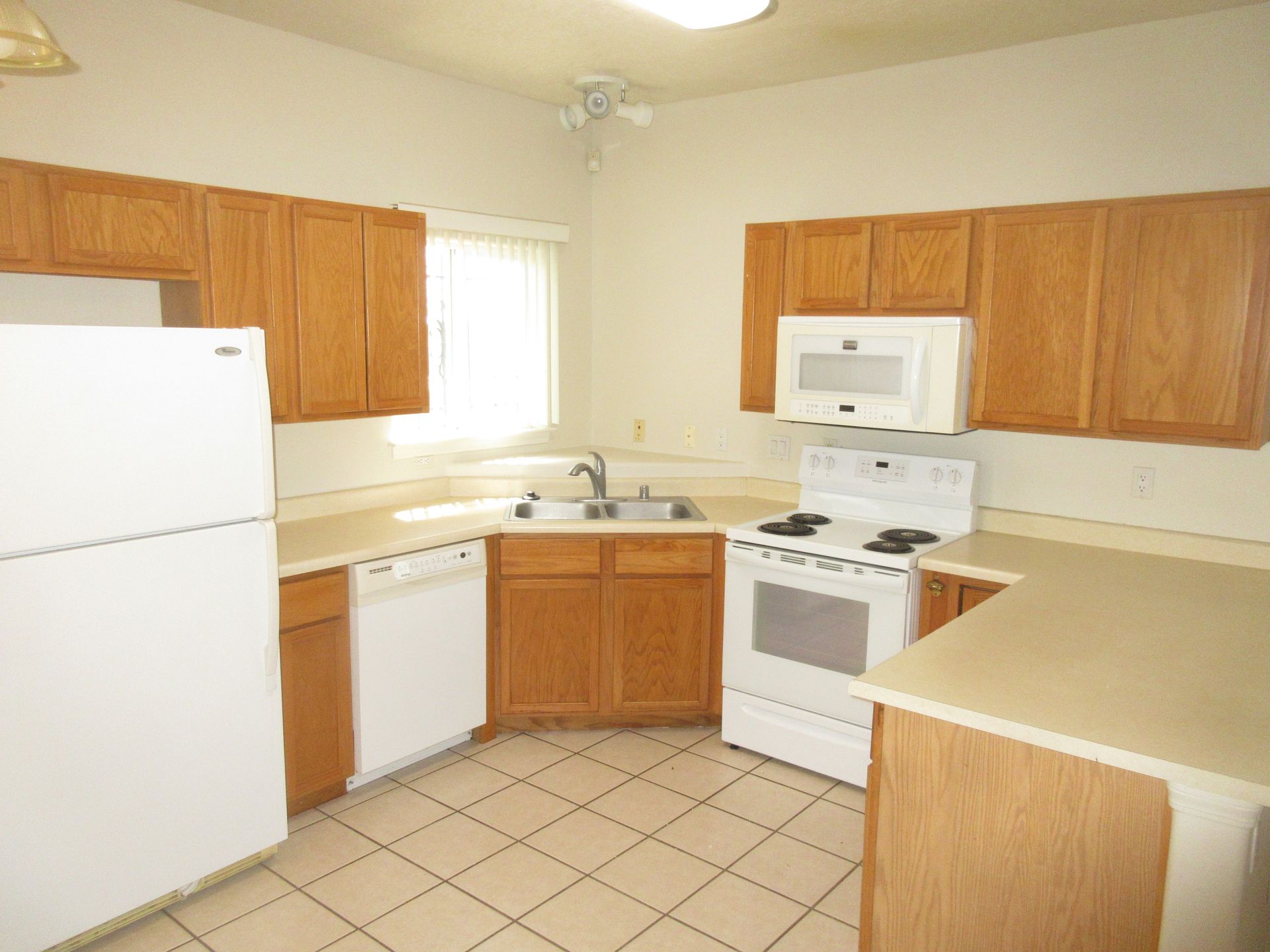 An empty kitchen with wooden cabinets and white appliances