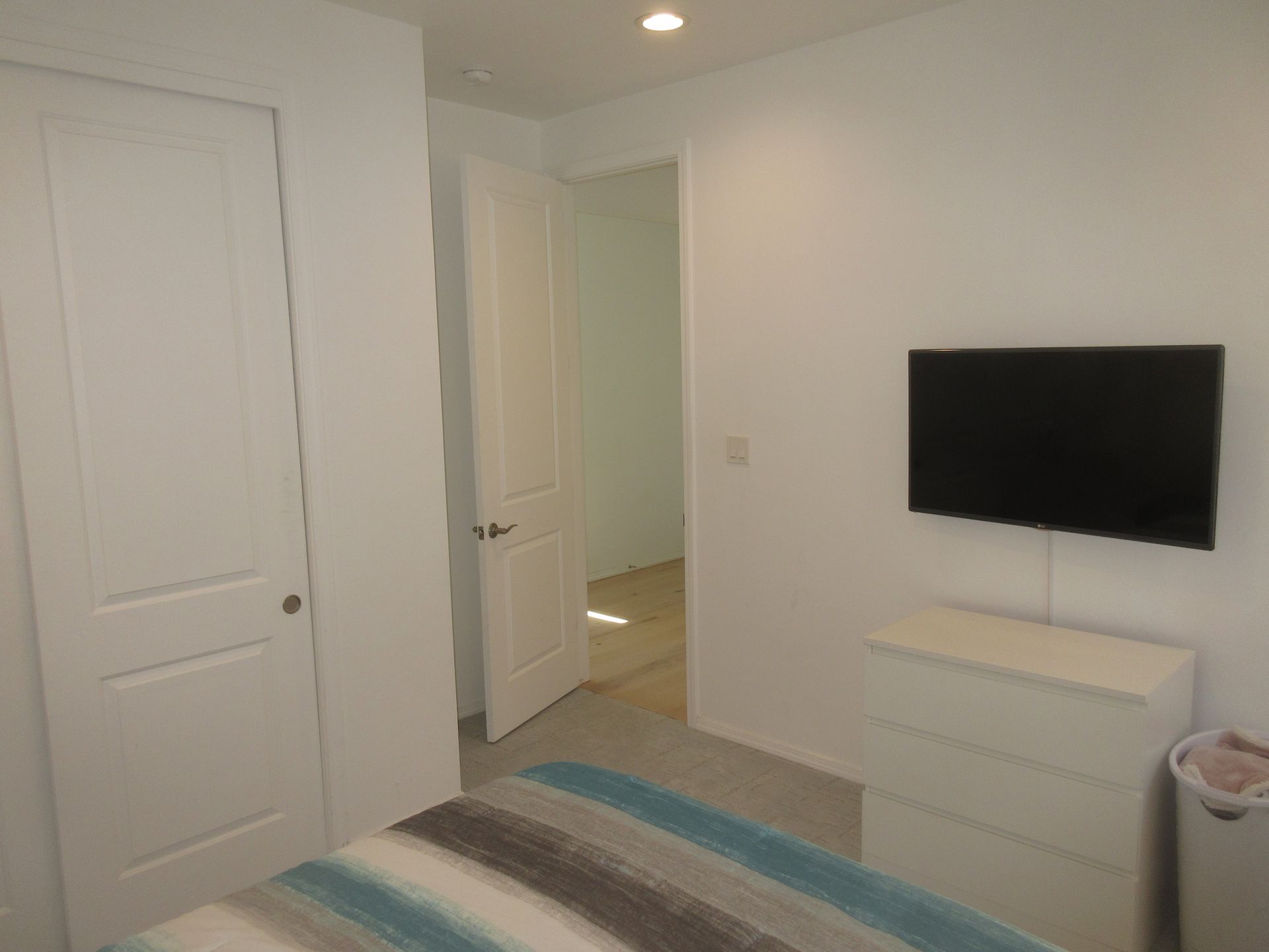 A bedroom with a bed , dresser and television on the wall.