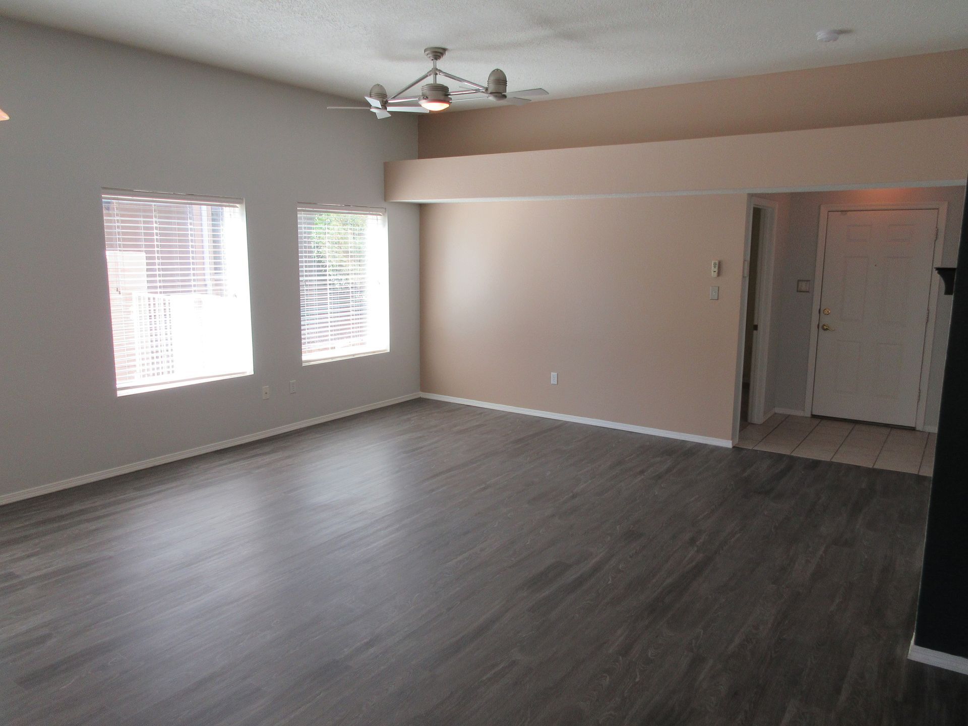 An empty living room with hardwood floors and a ceiling fan.