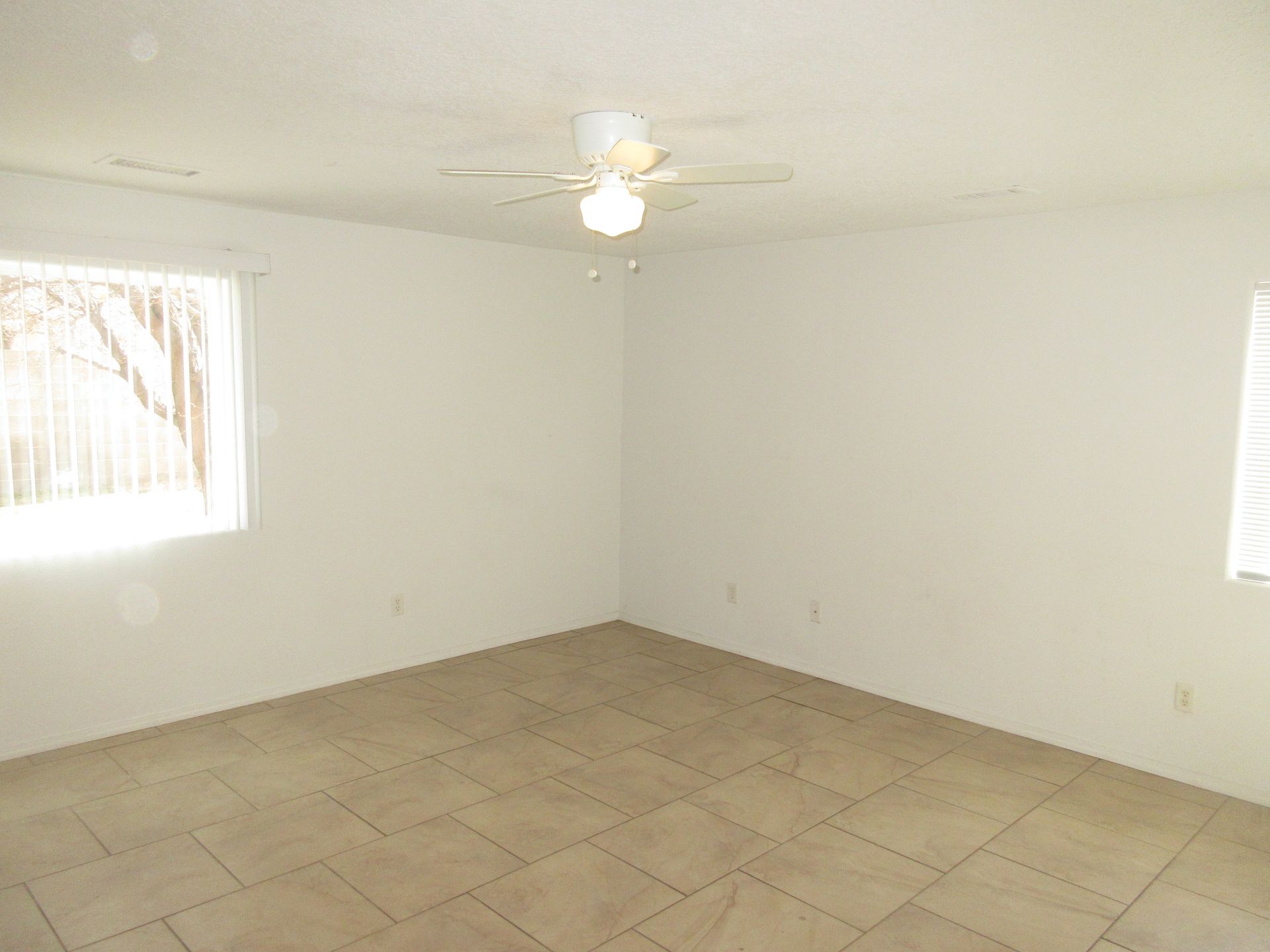 An empty room with a ceiling fan and a window.