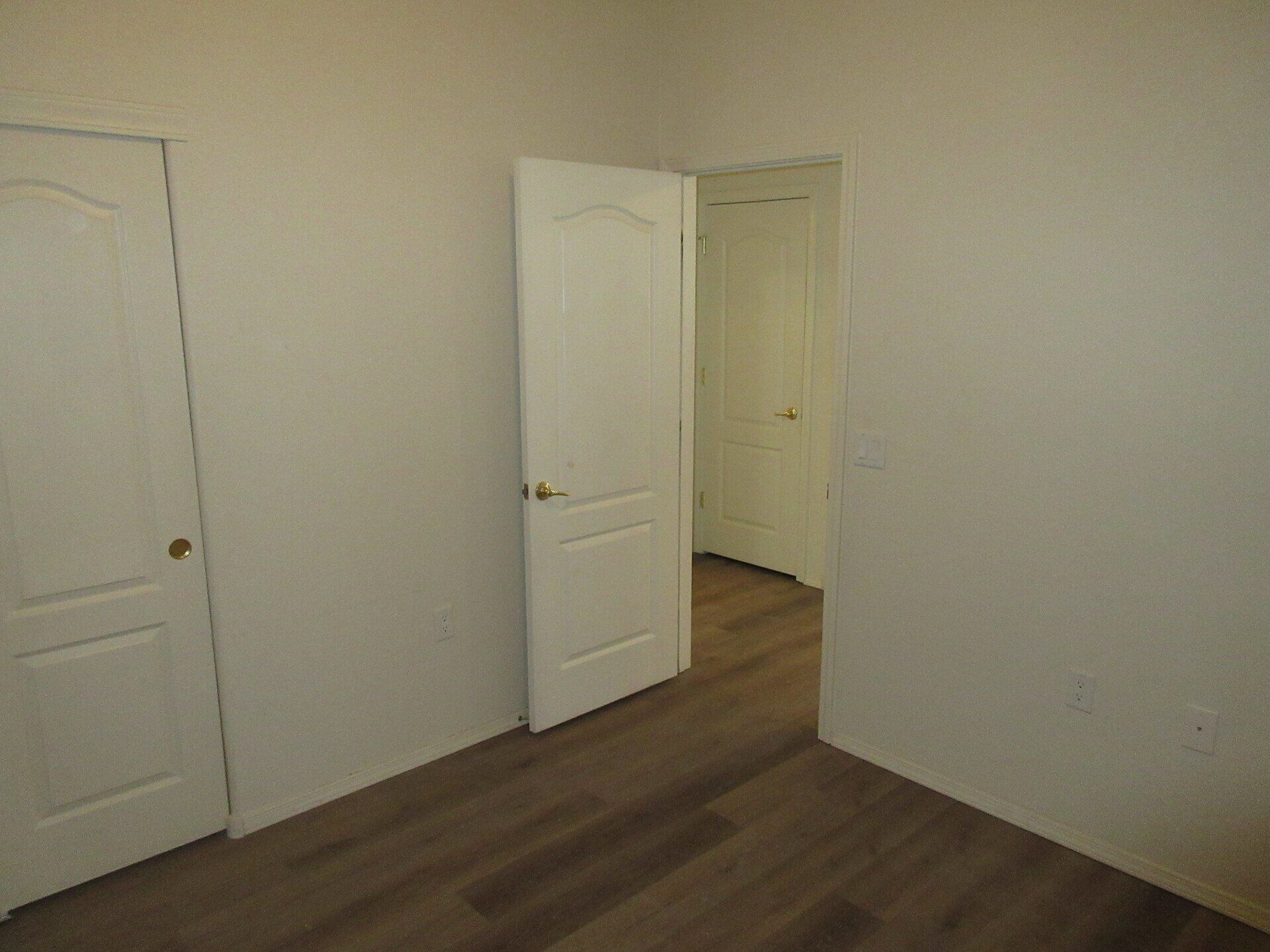 An empty room with two white doors and a wooden floor.