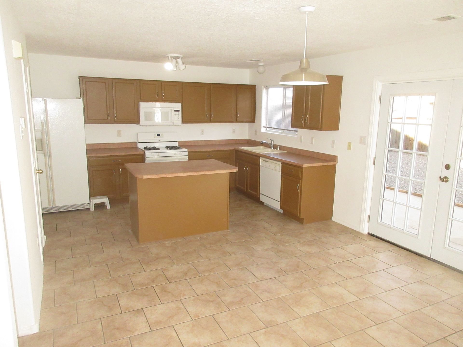 An empty kitchen with brown cabinets and white appliances
