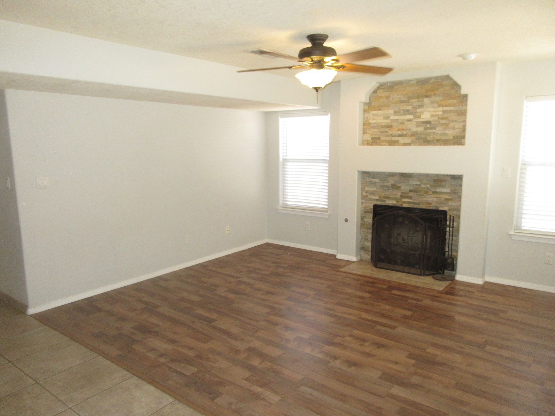 An empty living room with a fireplace and ceiling fan