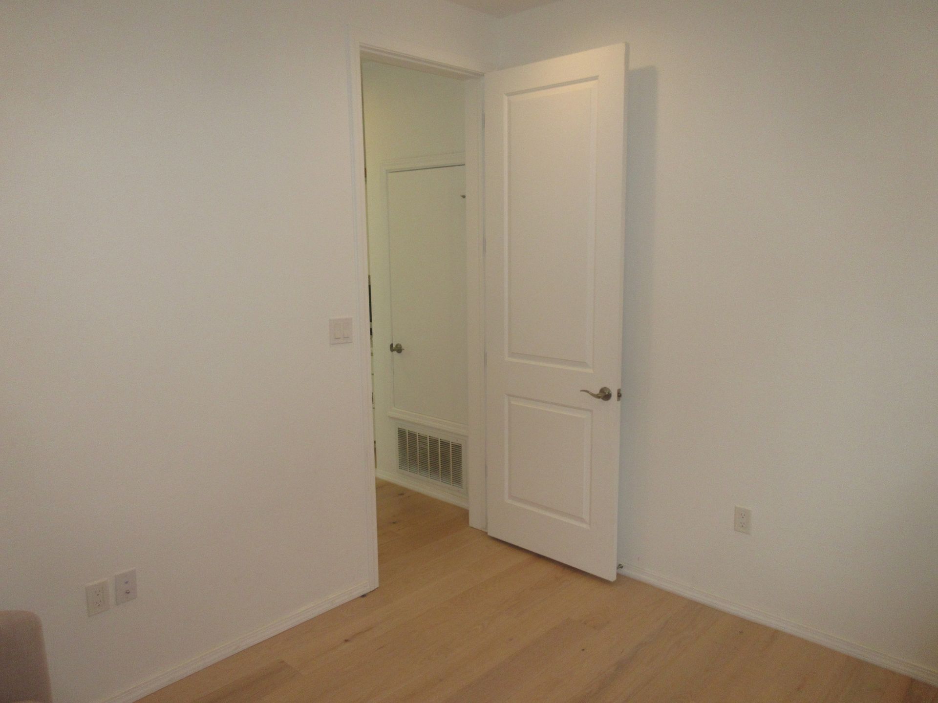 An empty room with a white door and a wooden floor.