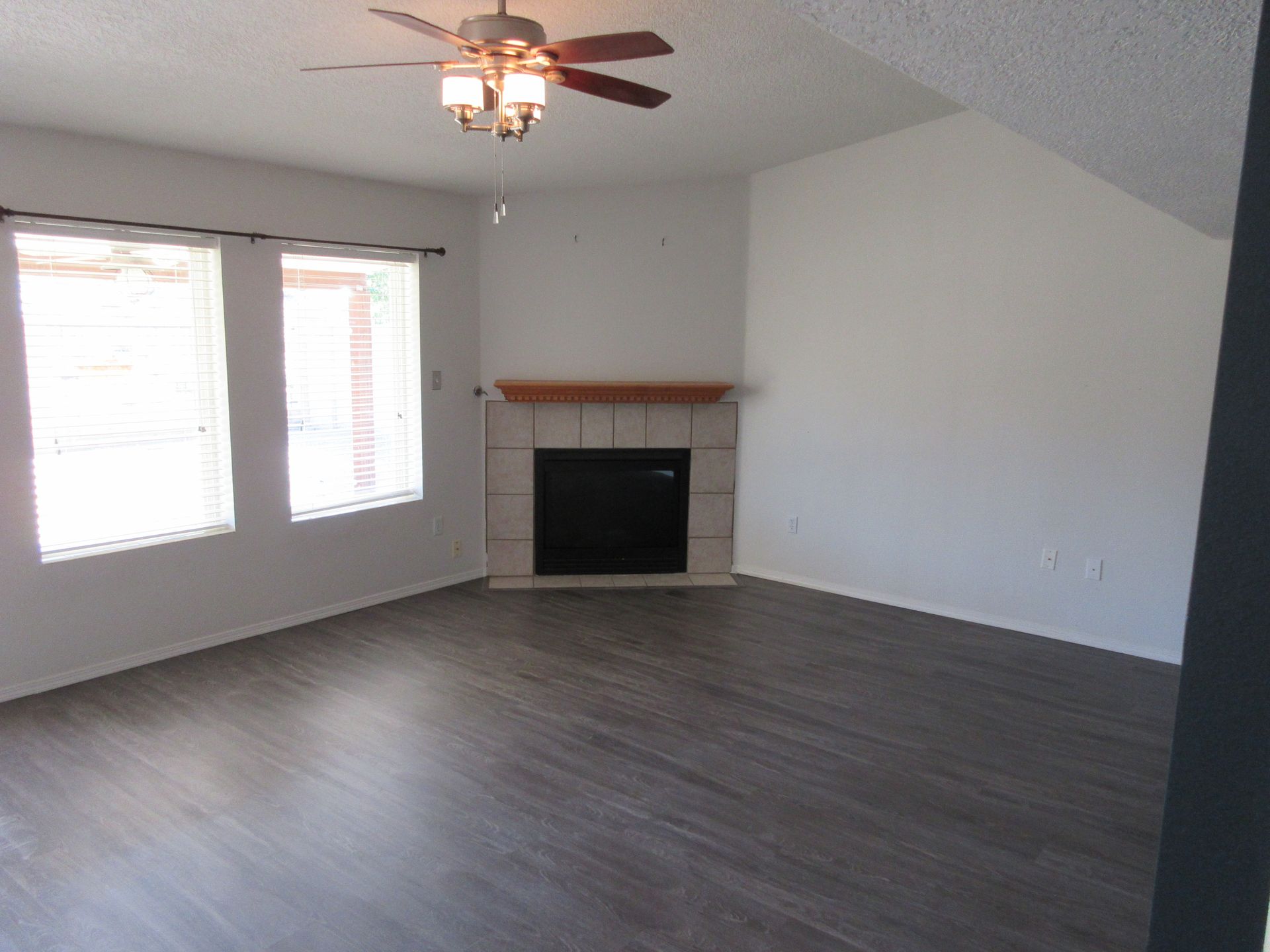 An empty living room with a fireplace and ceiling fan