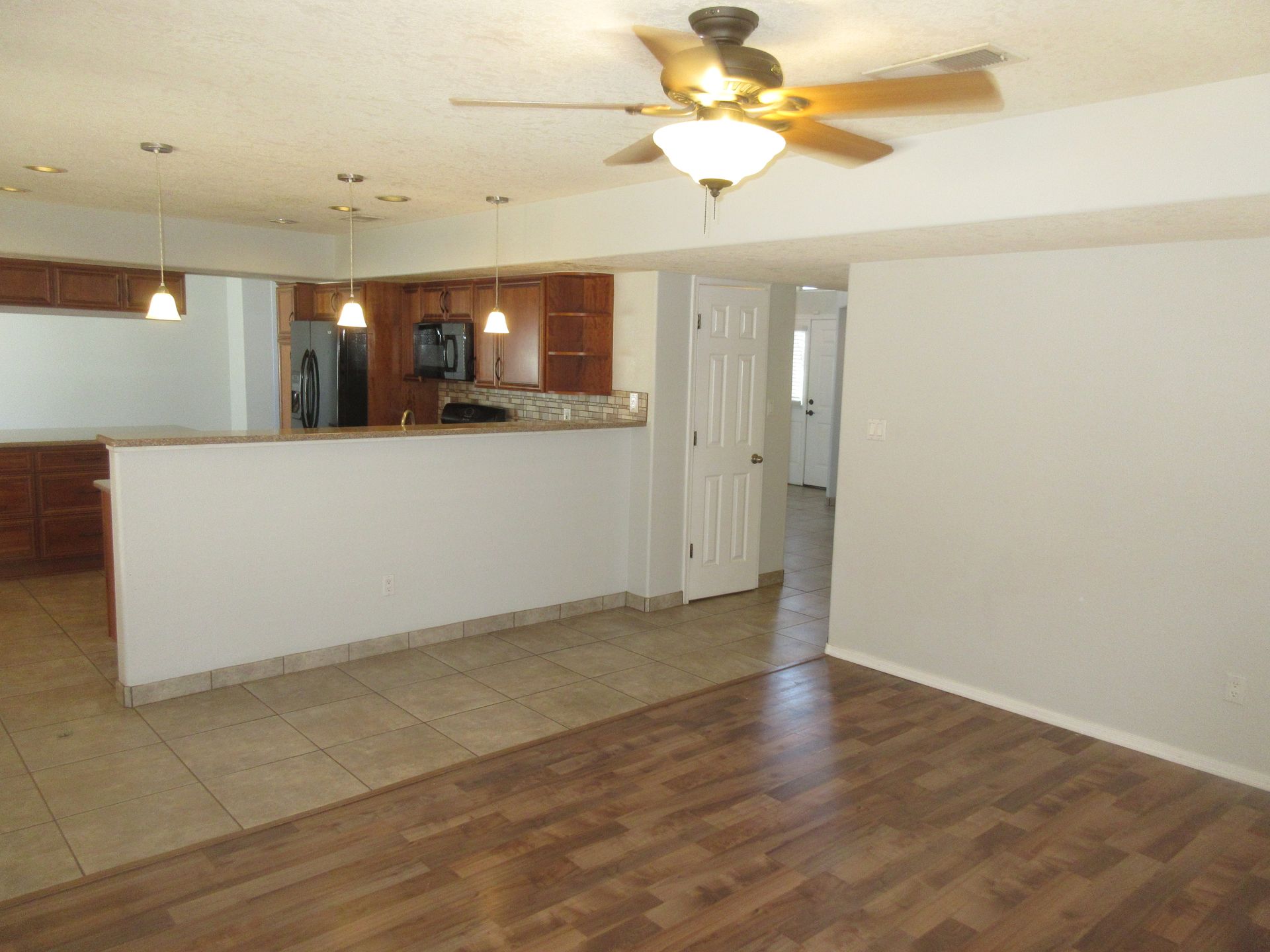 A living room with a ceiling fan and a kitchen in the background