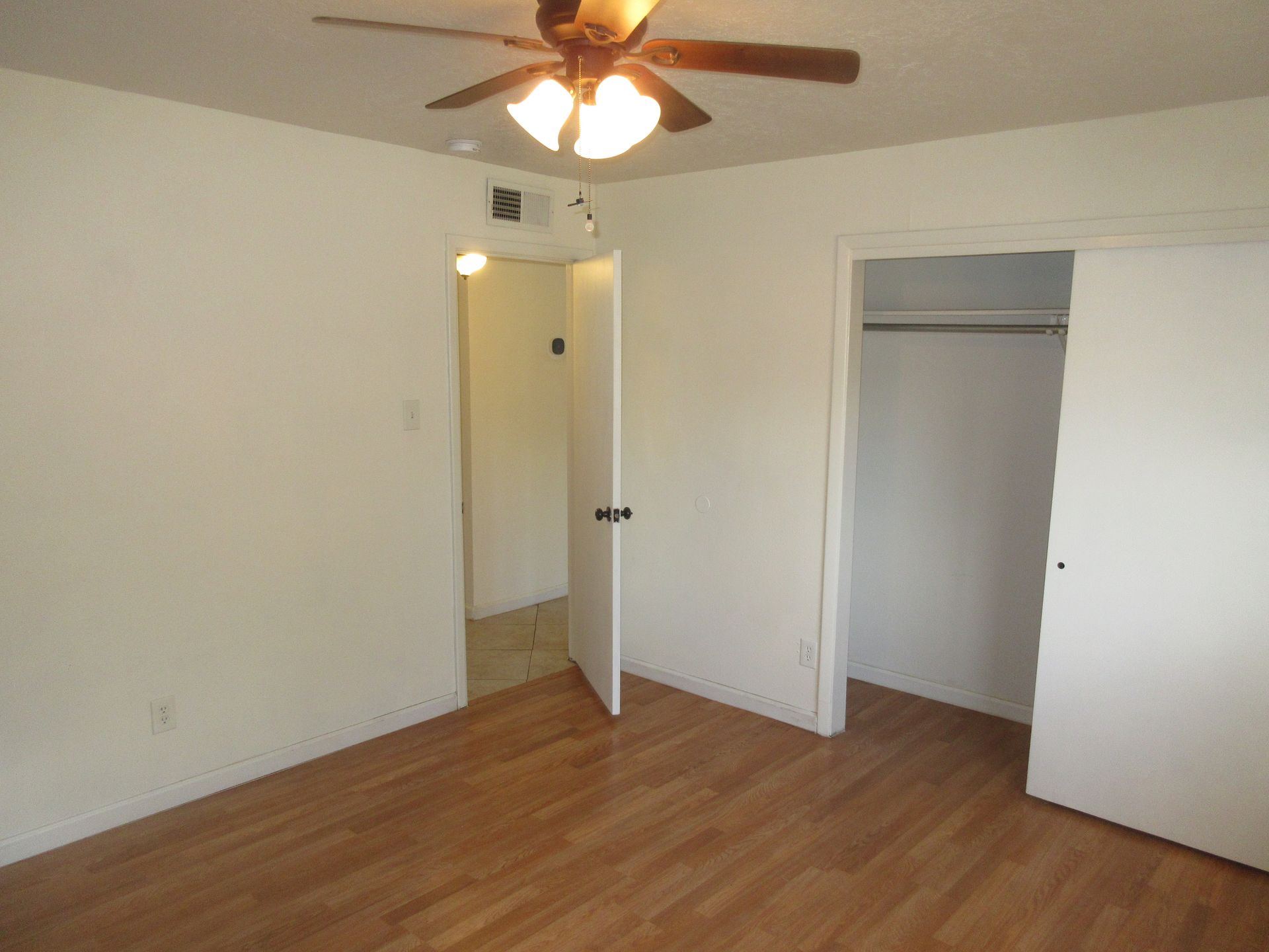 An empty bedroom with hardwood floors and a ceiling fan