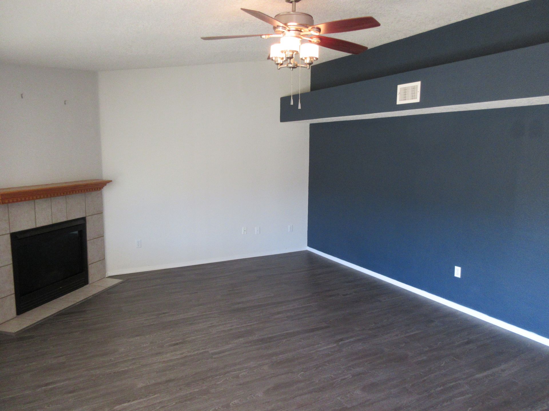 An empty living room with a fireplace and ceiling fan