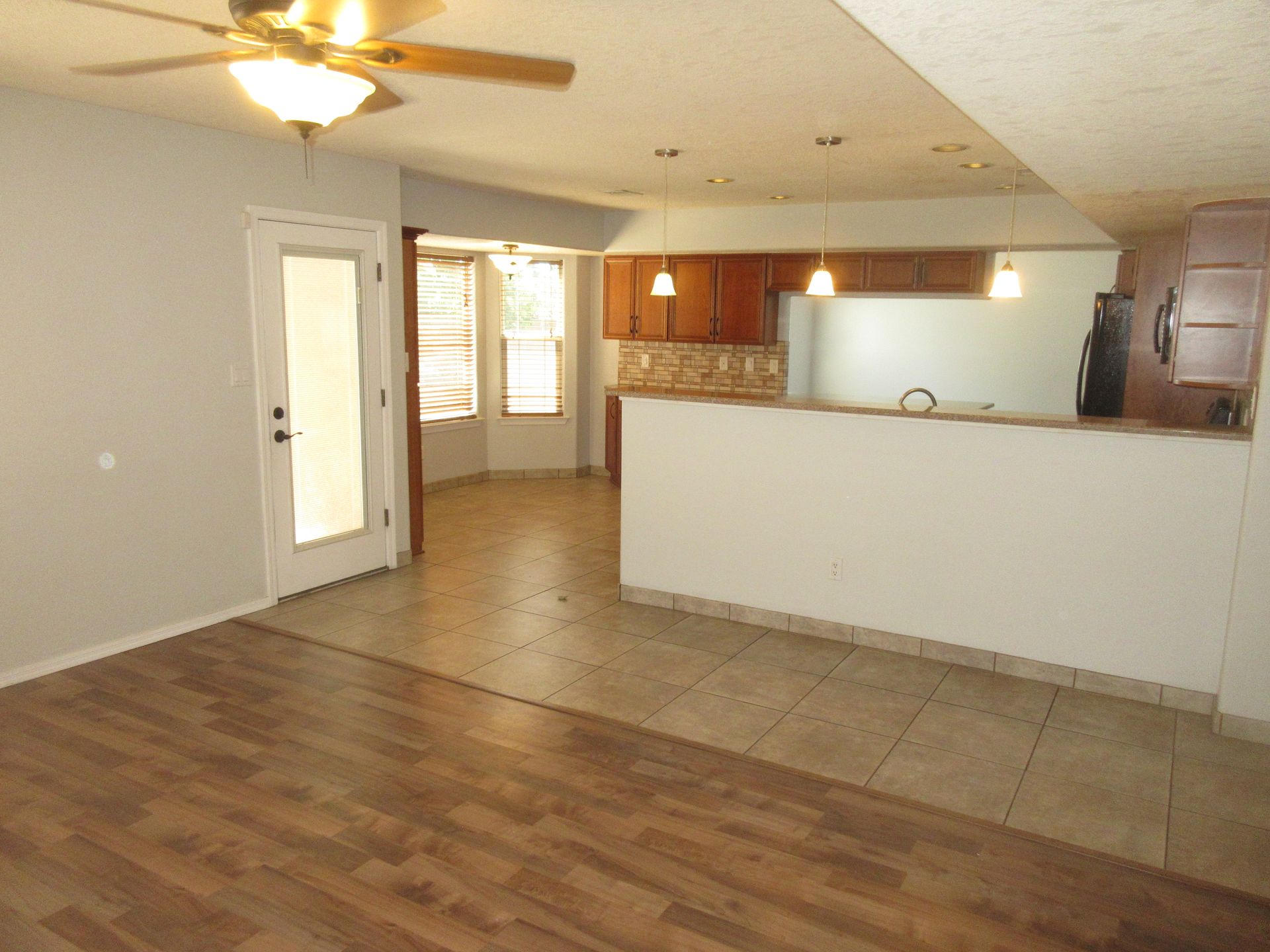 A living room with a ceiling fan and a kitchen in the background