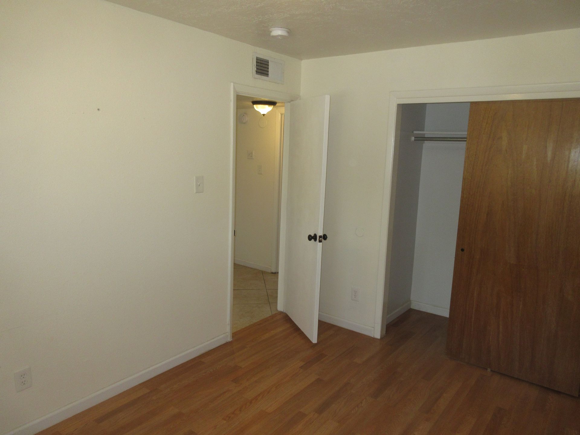 An empty bedroom with hardwood floors and a closet.