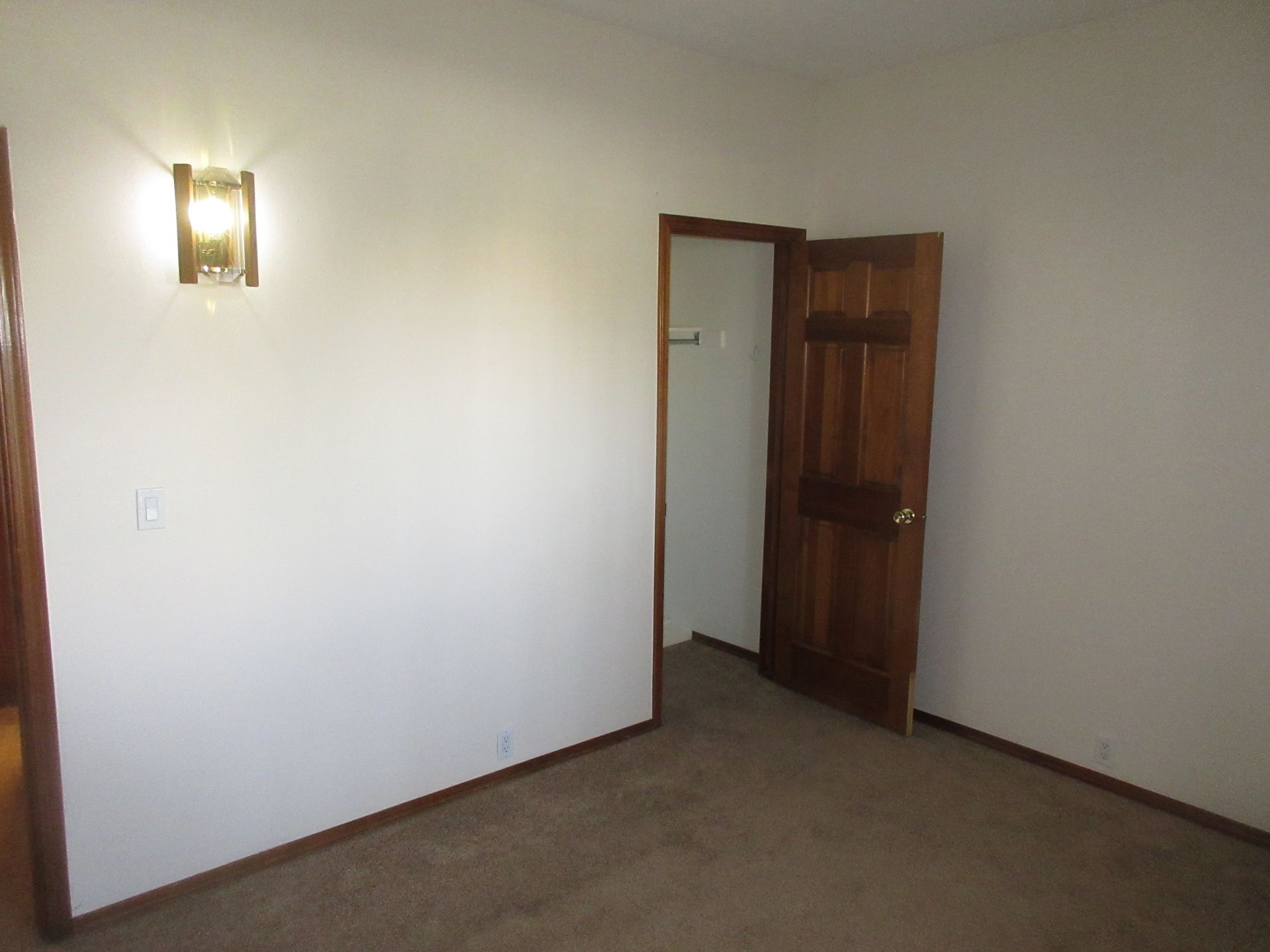 An empty bedroom with a wooden door and a light on the wall.