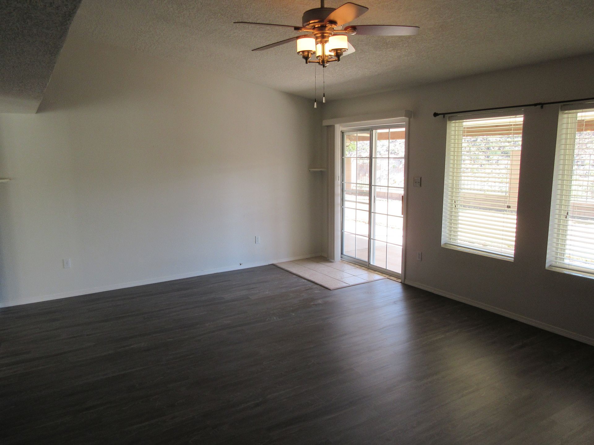 An empty living room with a ceiling fan and sliding glass doors