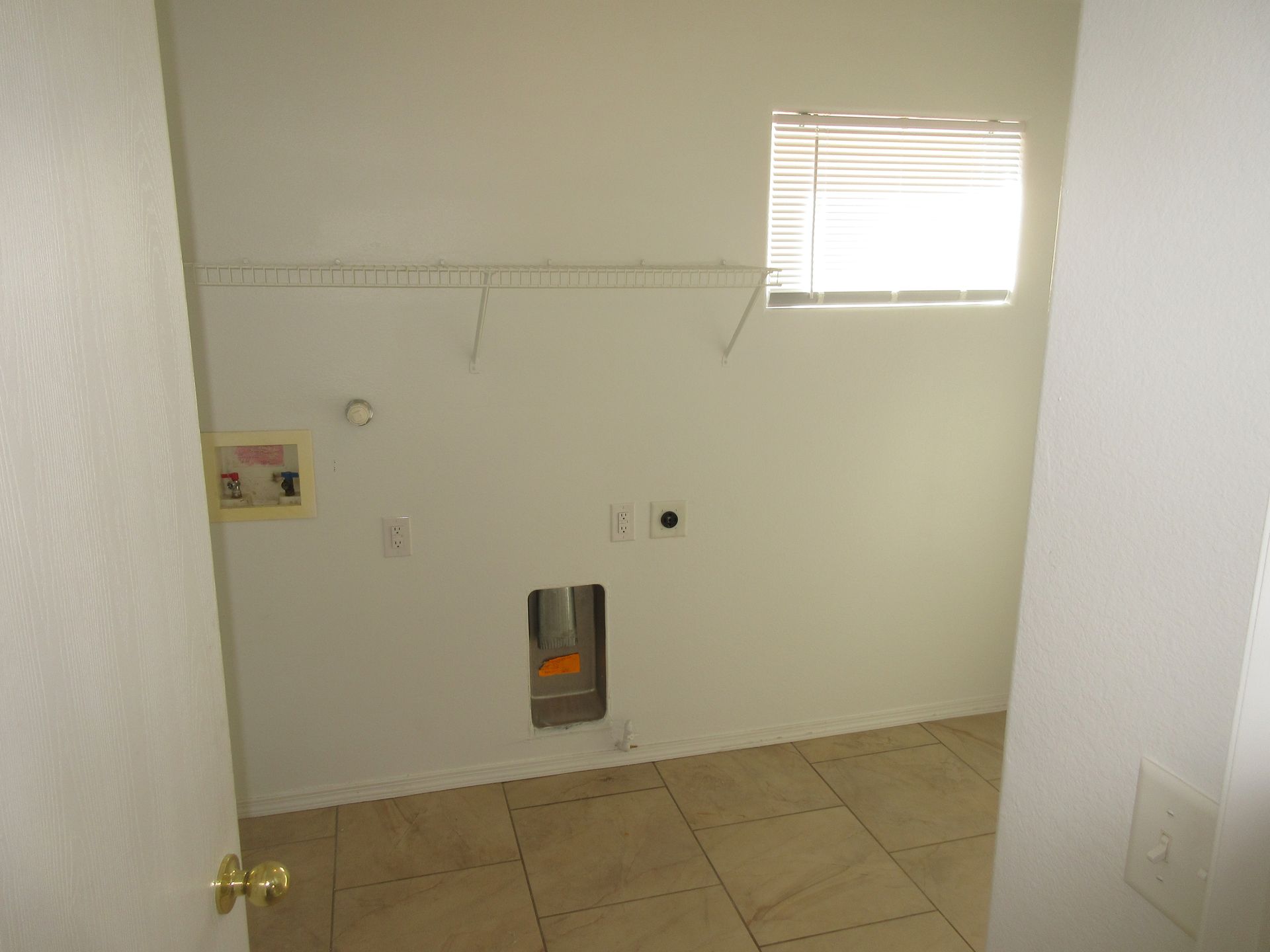 An empty laundry room with a window and a door.