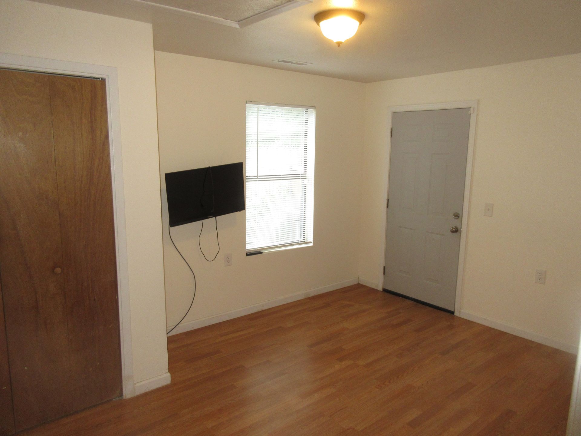 An empty room with hardwood floors and a television mounted on the wall