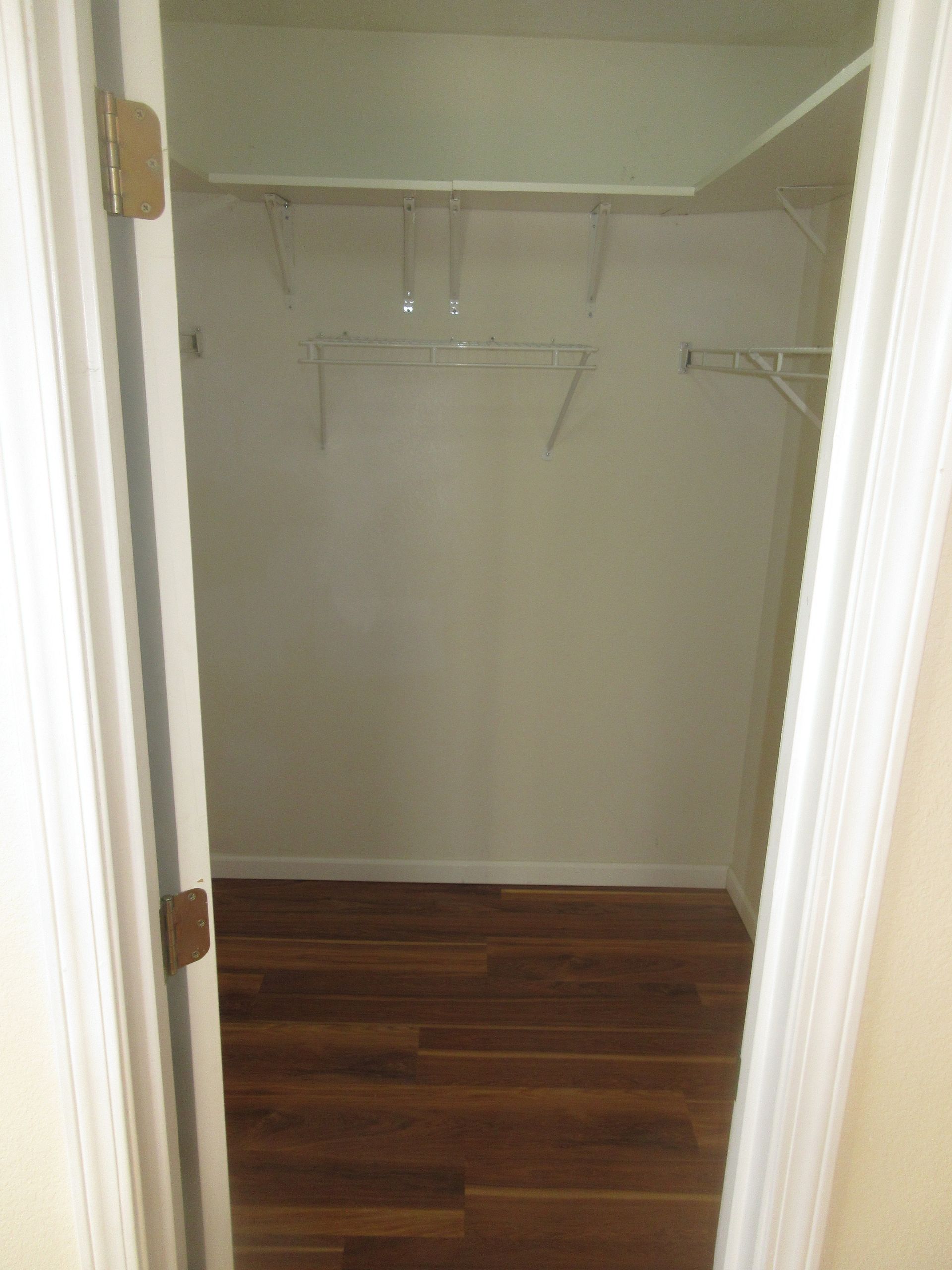 A walk in closet with hardwood floors and white walls