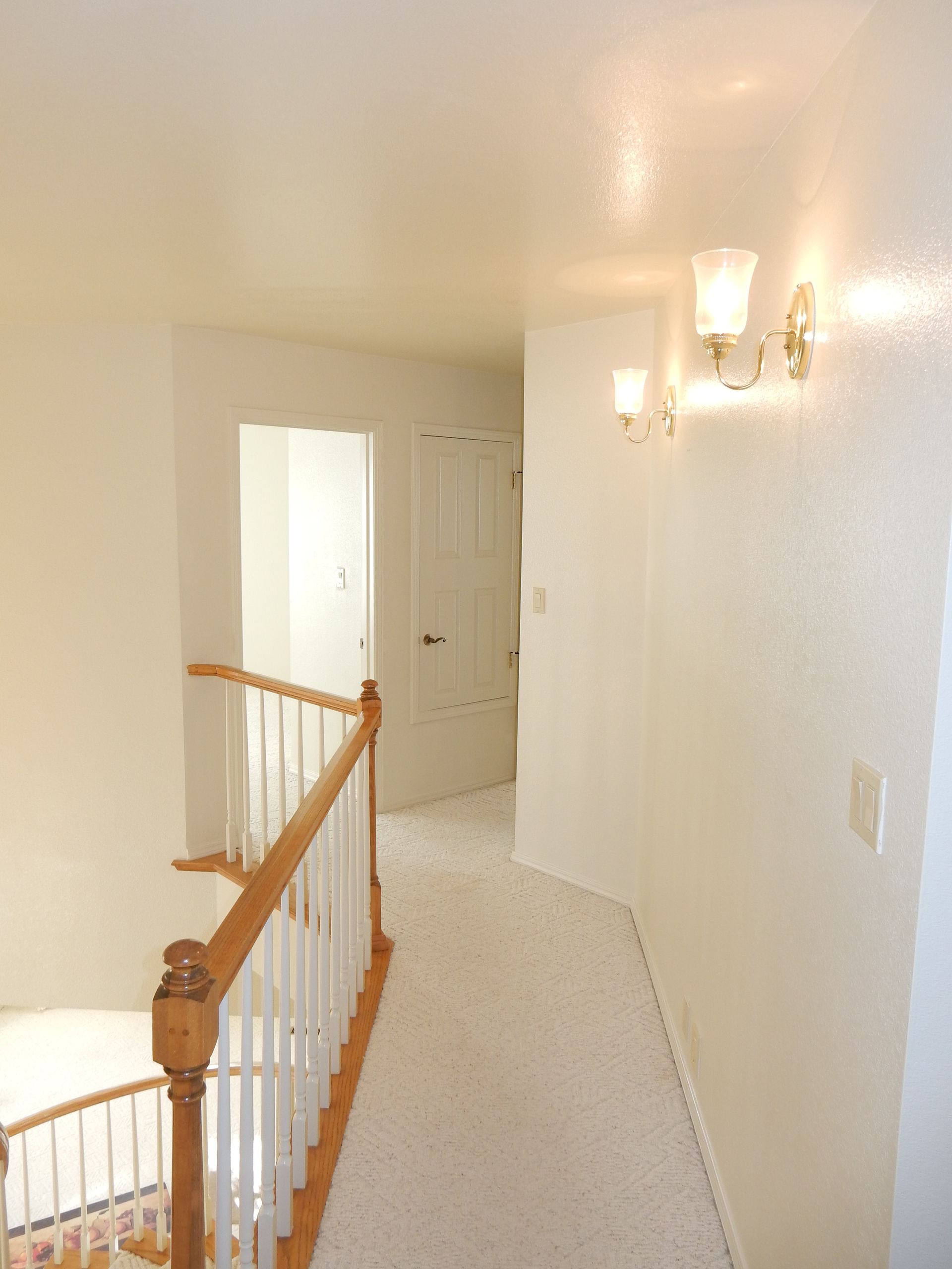 A hallway with white walls and a wooden railing
