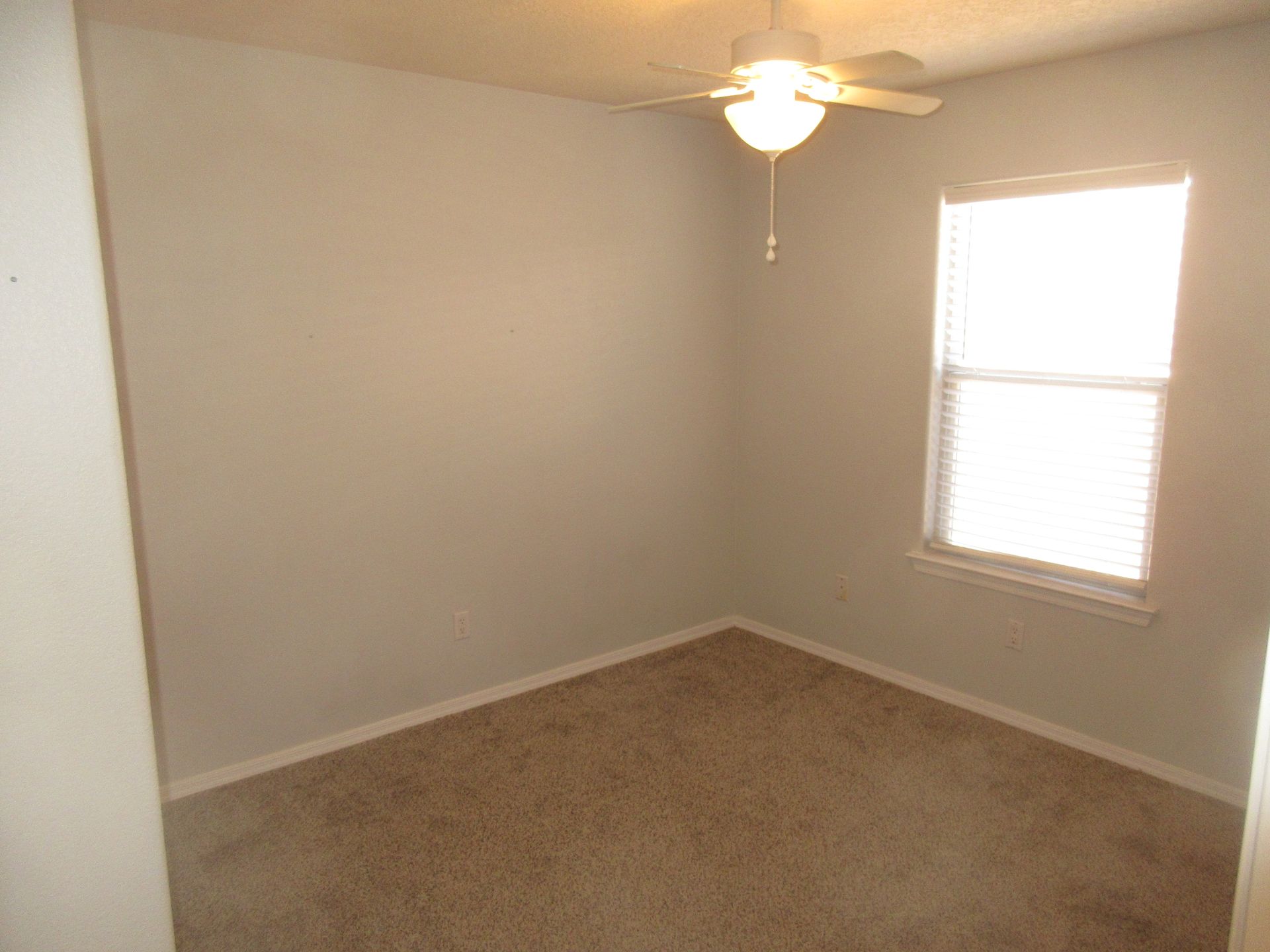 An empty bedroom with a ceiling fan and a window.