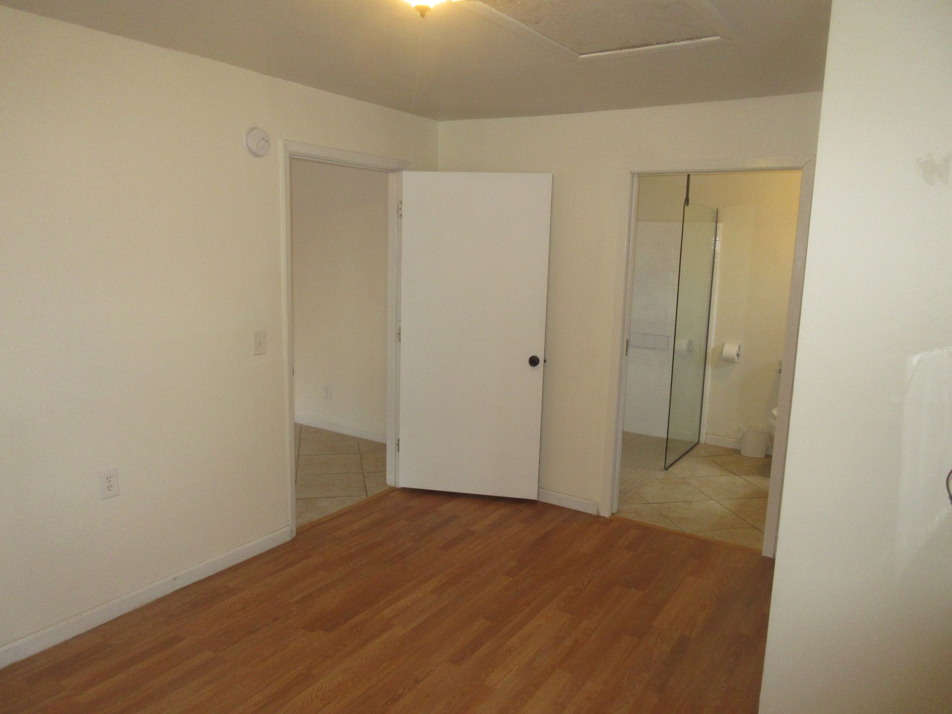 An empty room with hardwood floors and a white door leading to a bathroom.