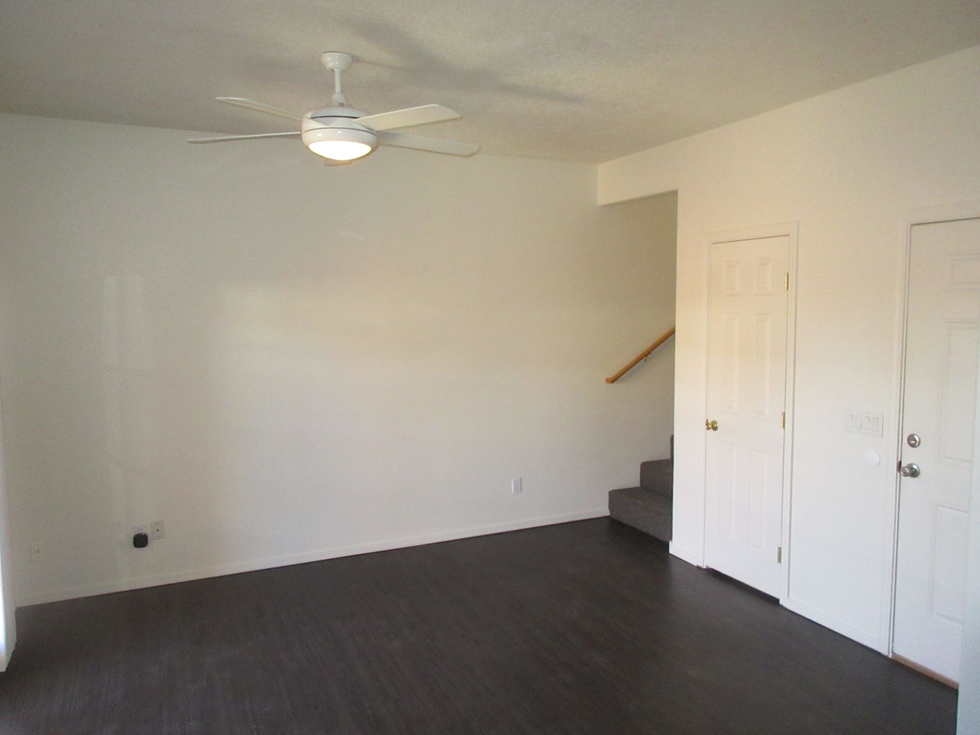 An empty living room with a ceiling fan and stairs
