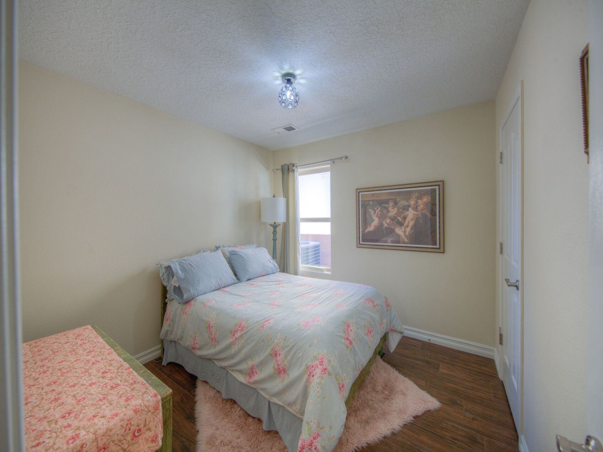 A bedroom with a bed , dresser , lamp and window.