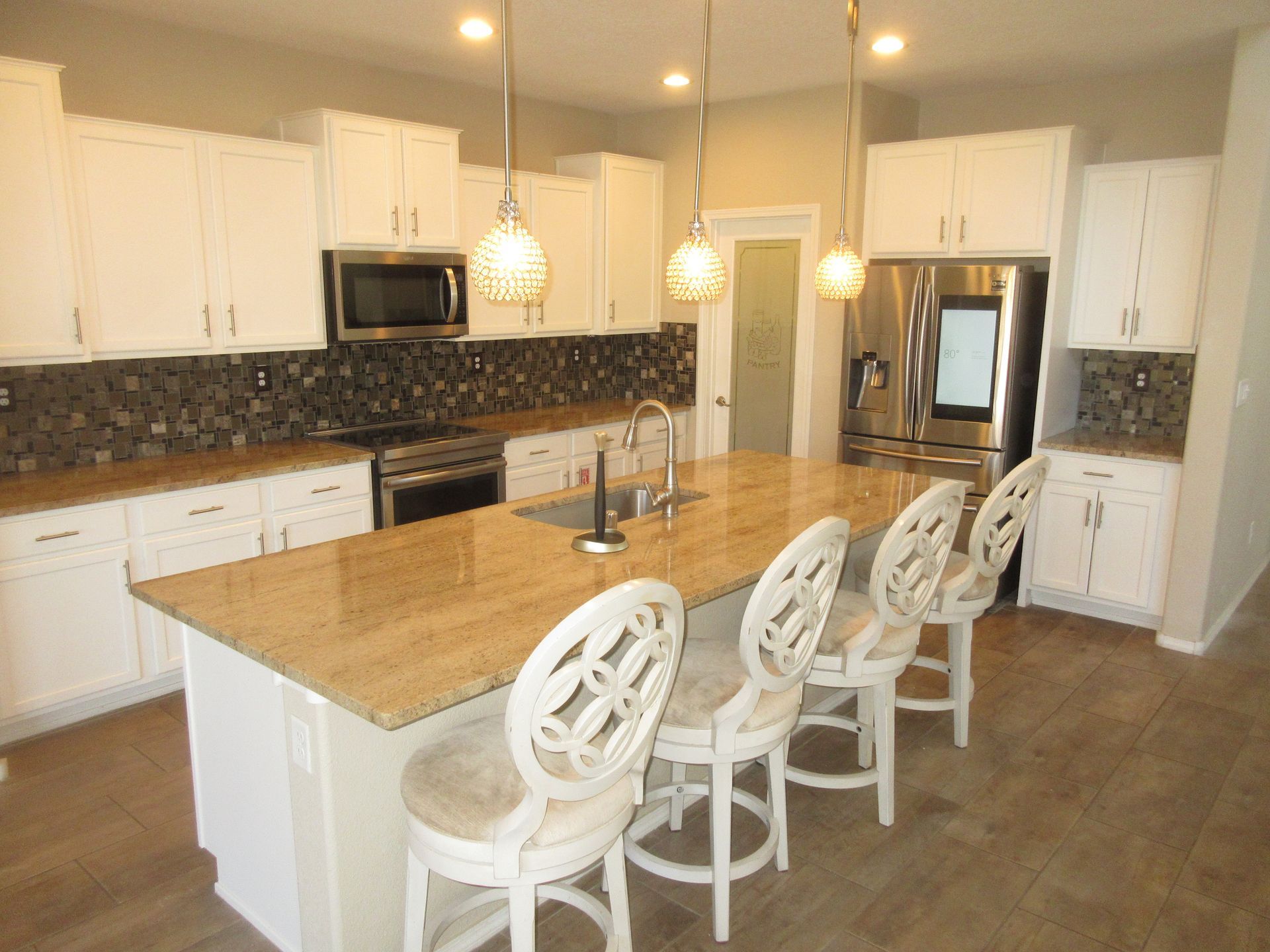 A kitchen with white cabinets , granite counter tops , stainless steel appliances and a large island.
