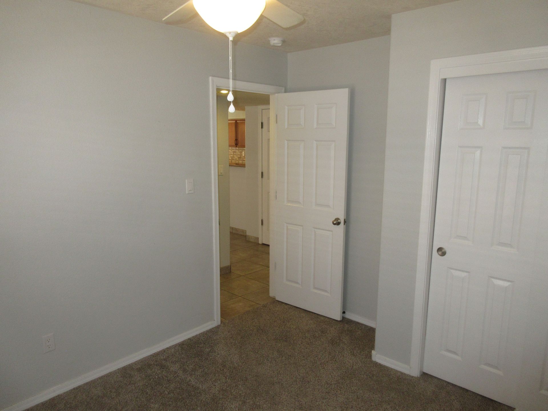 An empty bedroom with a ceiling fan and two doors.