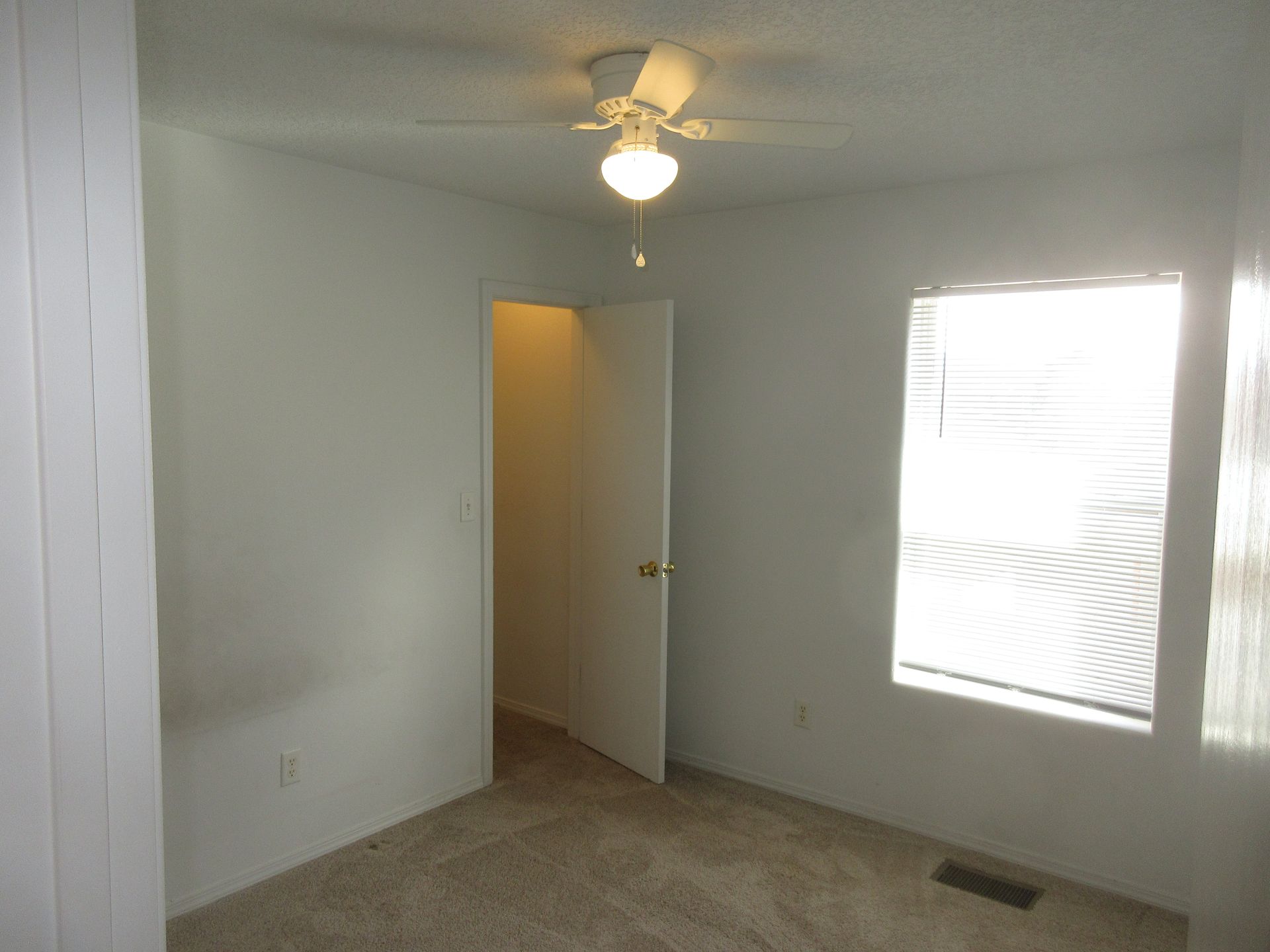 An empty bedroom with a ceiling fan and a window
