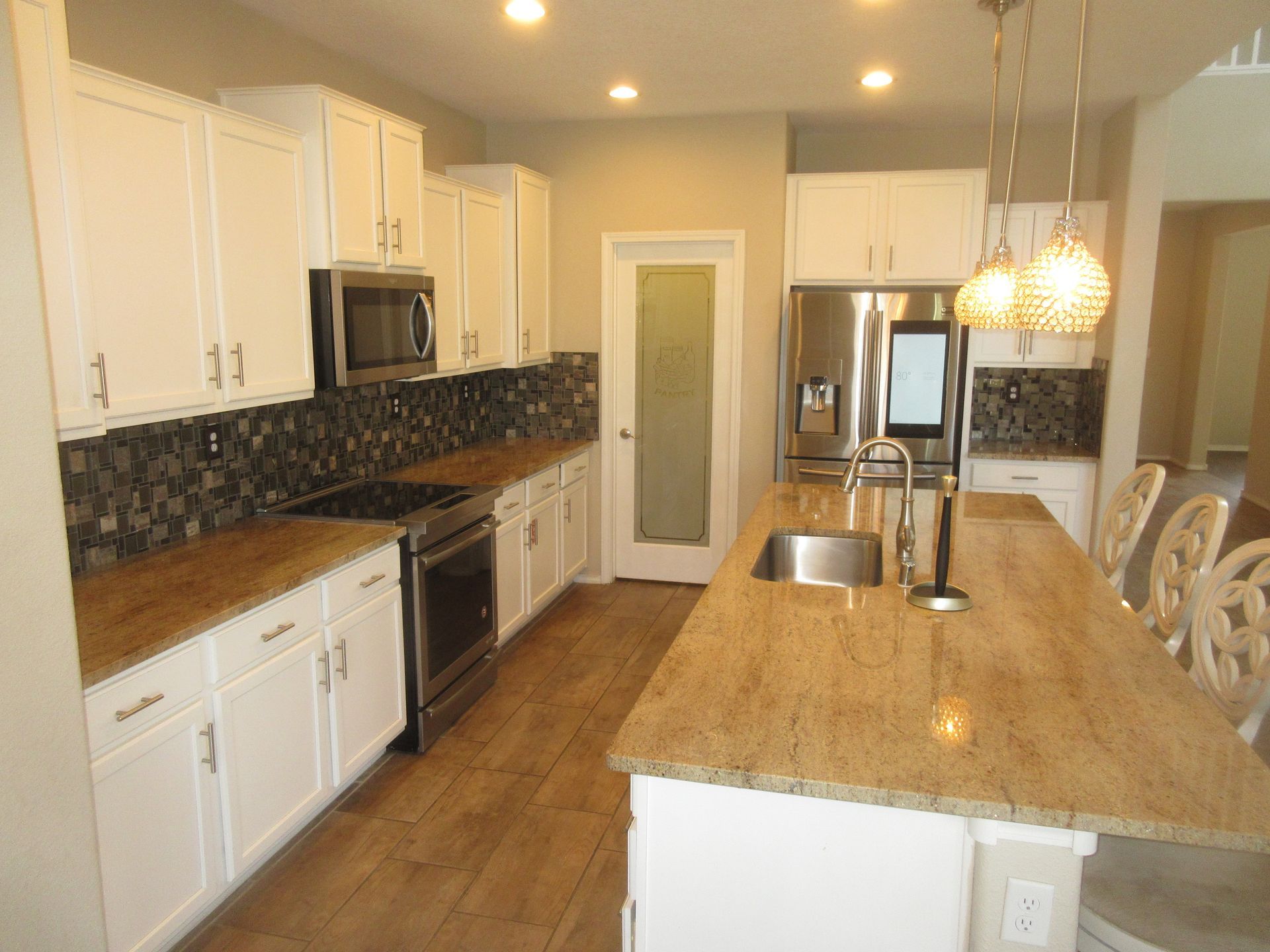 A kitchen with white cabinets , granite counter tops , stainless steel appliances and a large island.