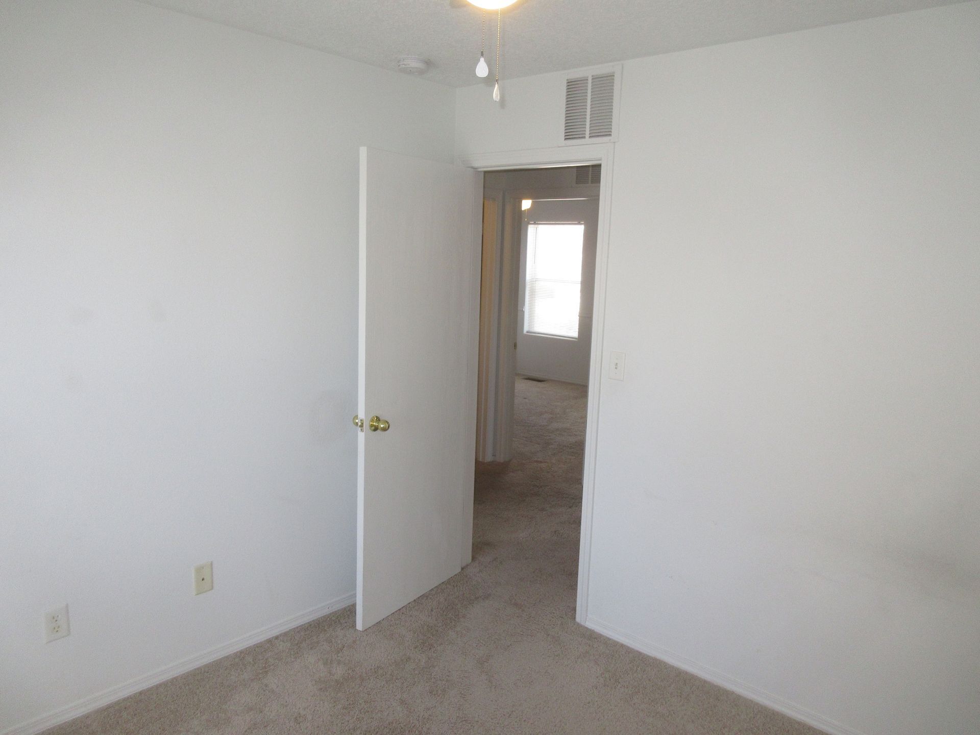 An empty bedroom with a door open and a window.