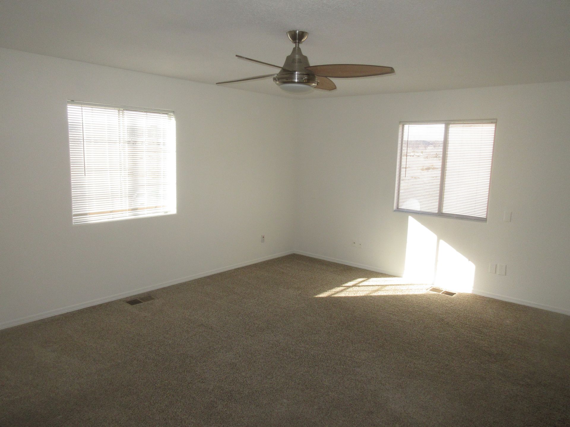 An empty room with a ceiling fan and two windows