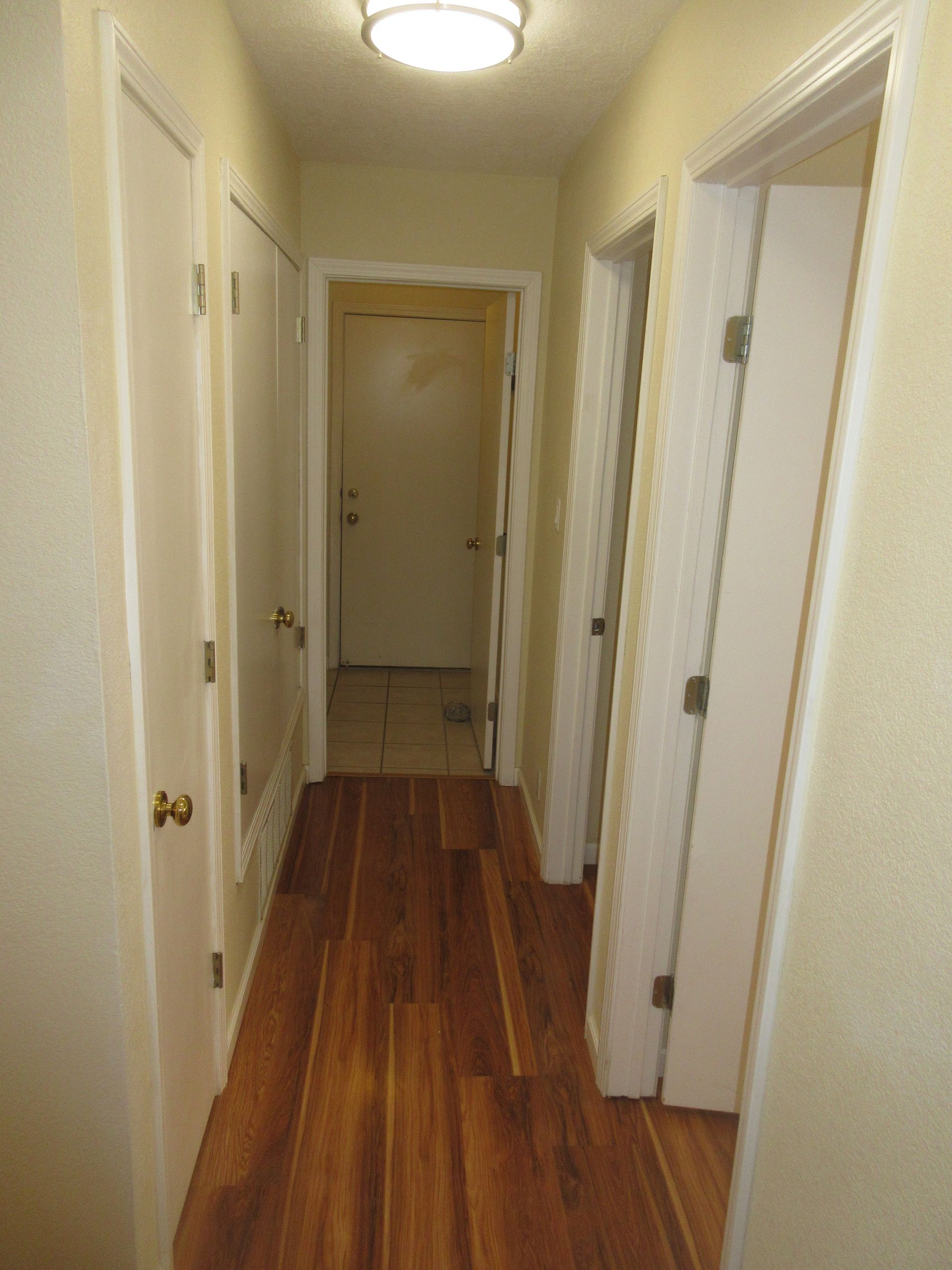 A hallway with hardwood floors and white doors leading to a doorway.
