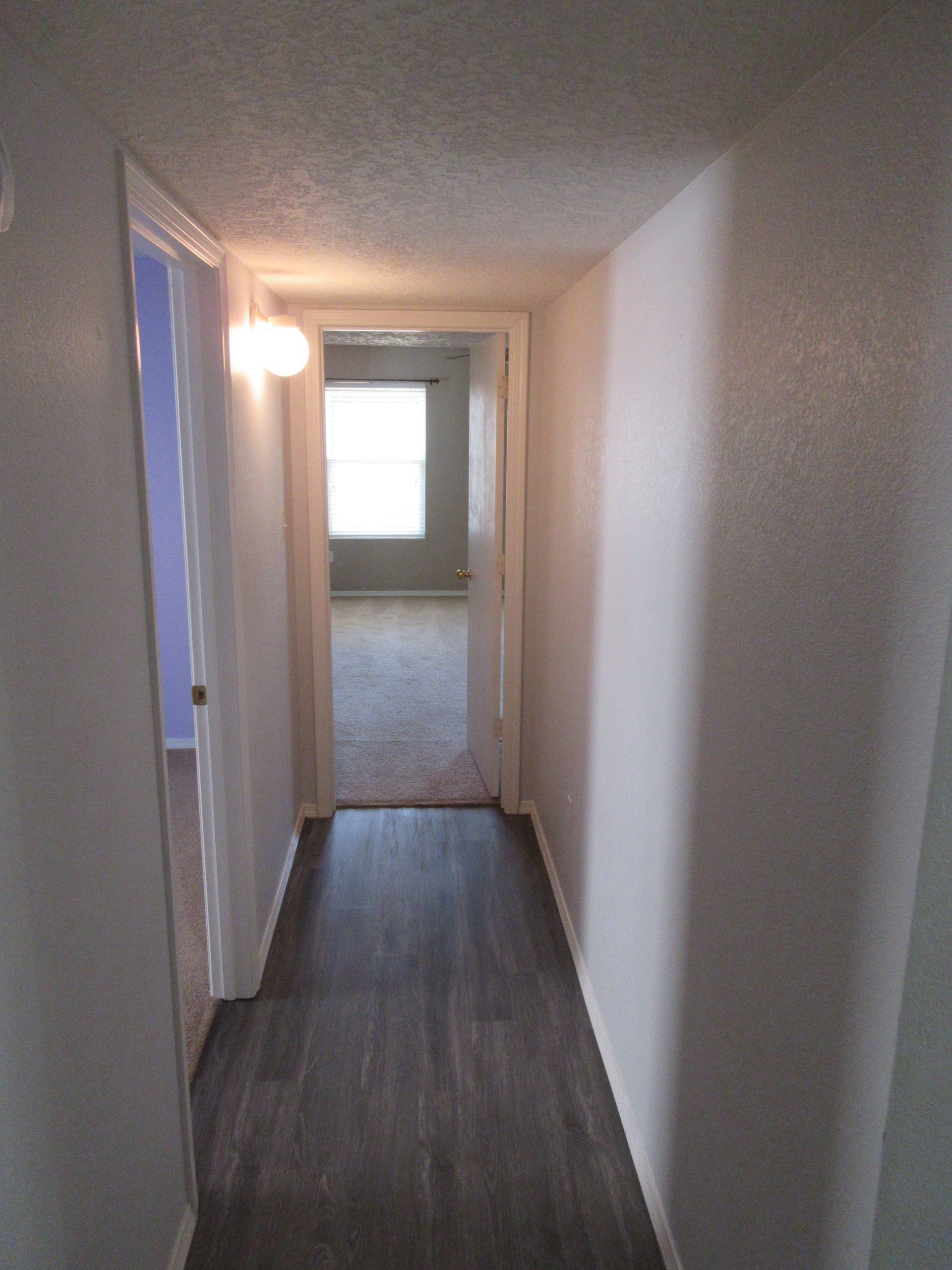 A hallway with hardwood floors and white walls leading to a living room.