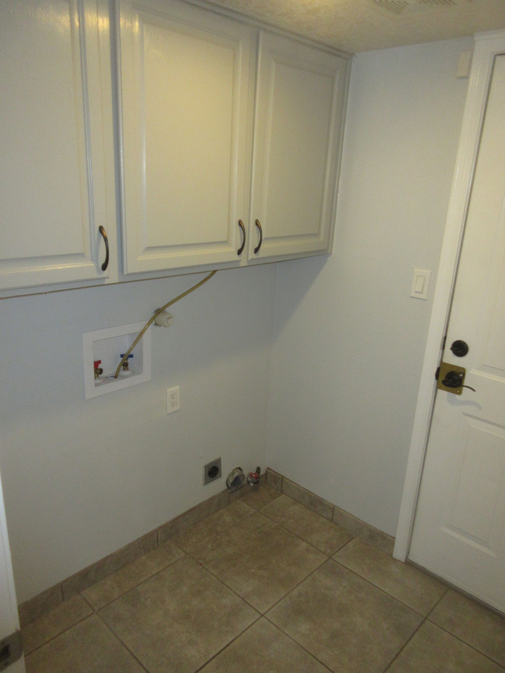 A laundry room with white cabinets and a door