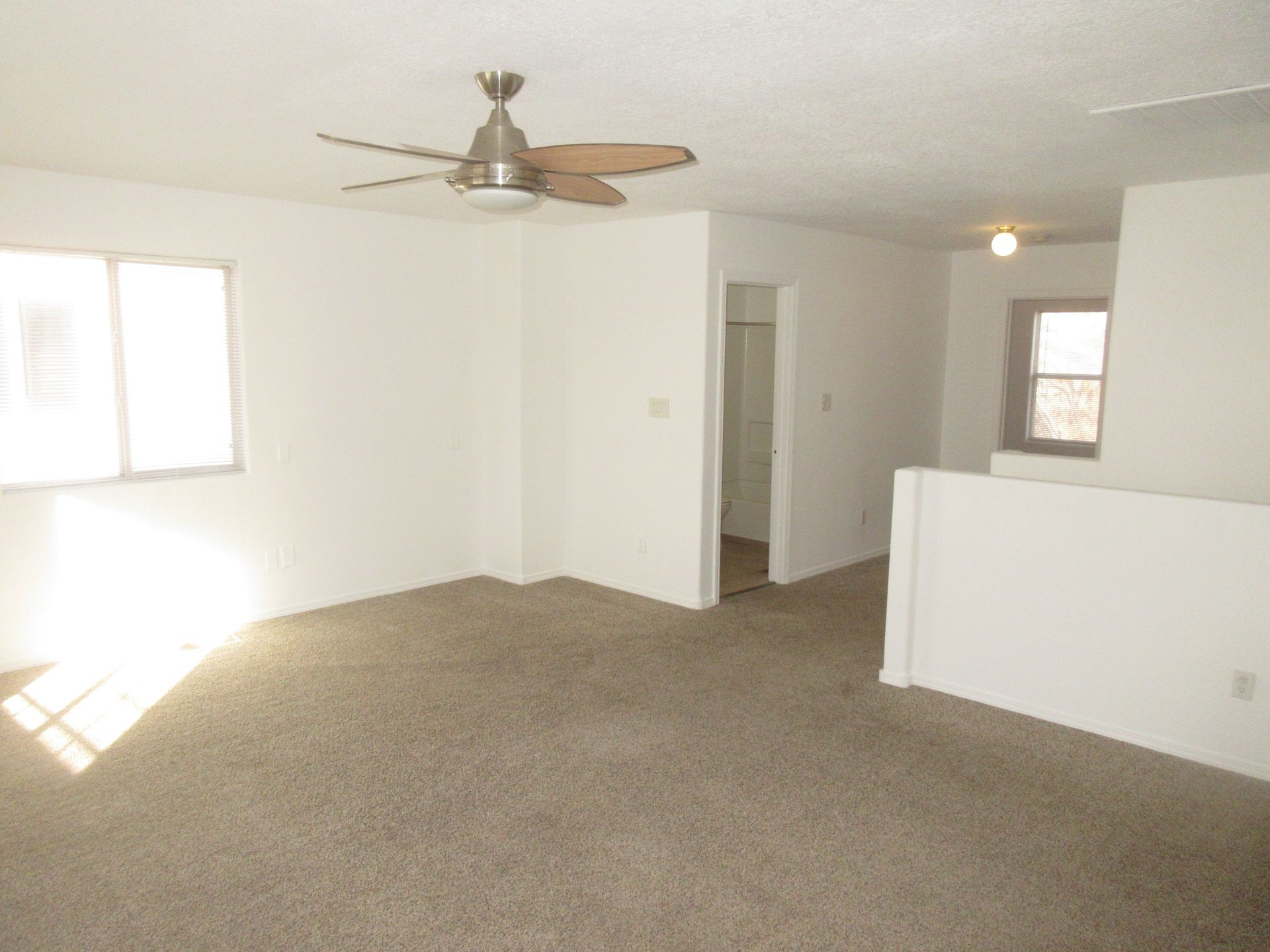An empty living room with a ceiling fan and a window