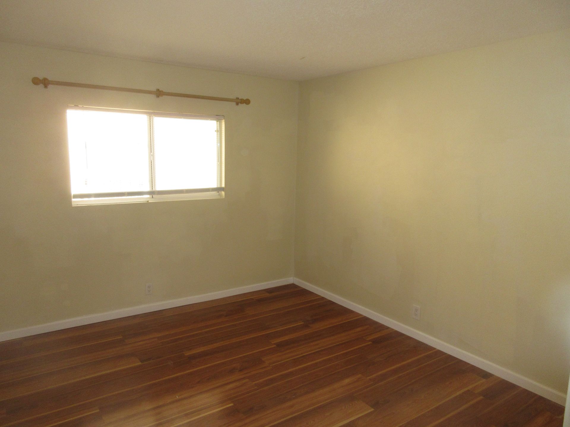 An empty bedroom with hardwood floors and a window.