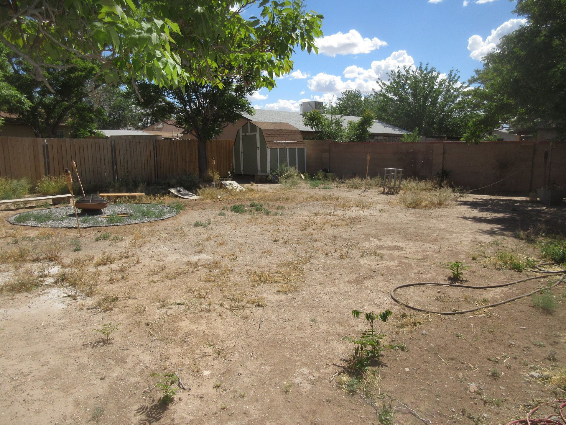 An empty backyard with a fence and a house in the background