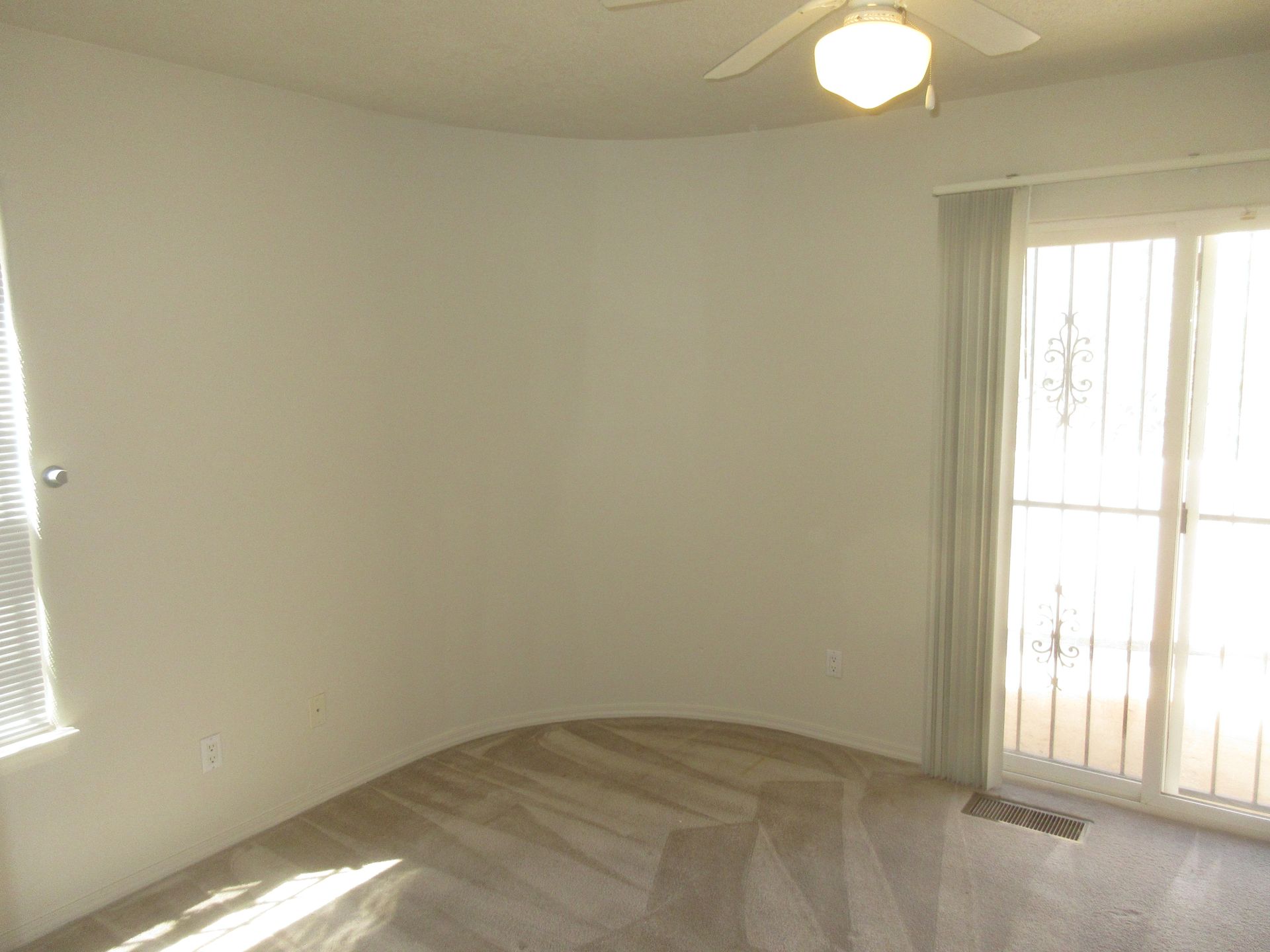 An empty room with a ceiling fan and sliding glass doors