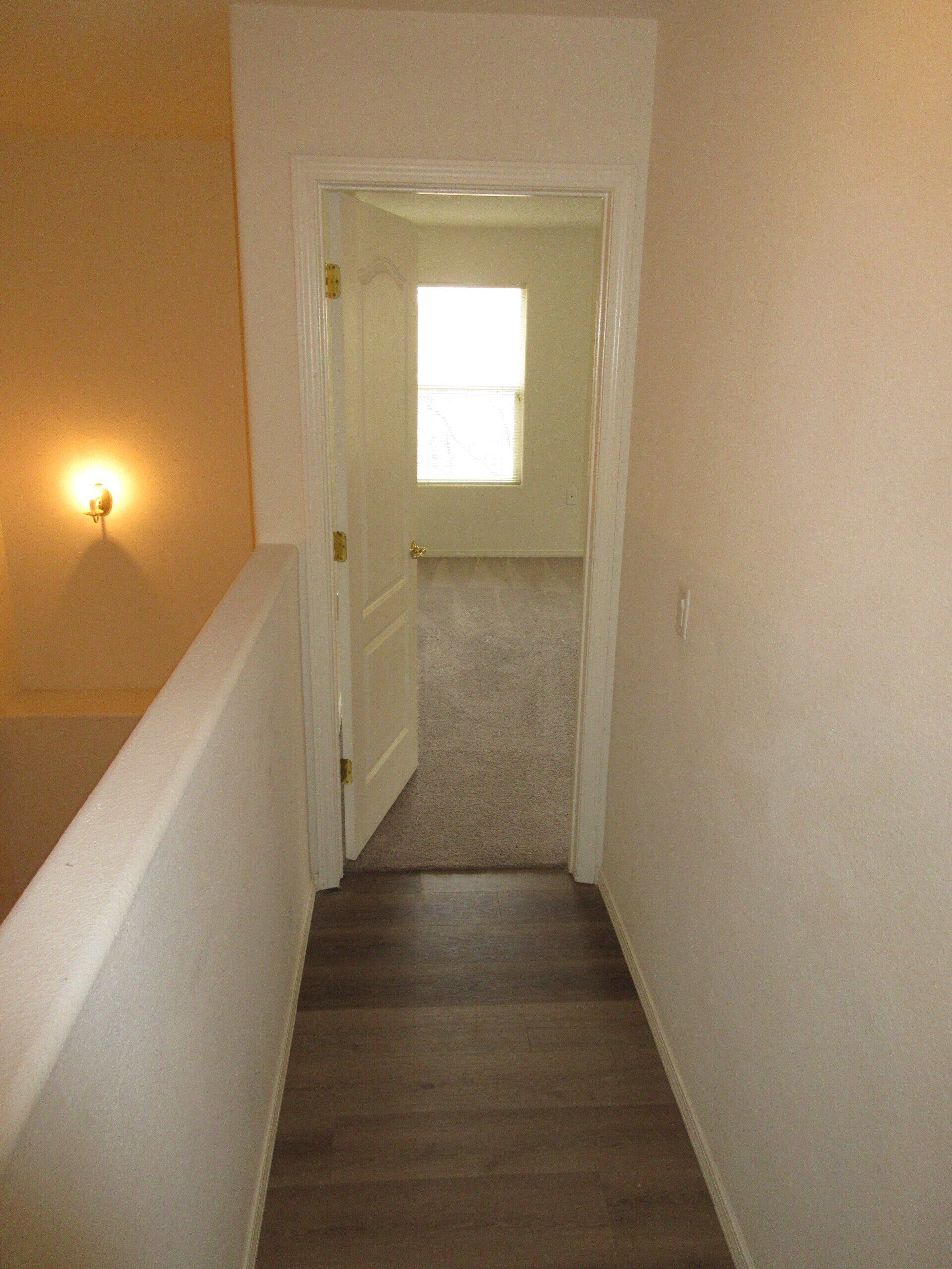 A hallway leading to a bedroom with a window and stairs.