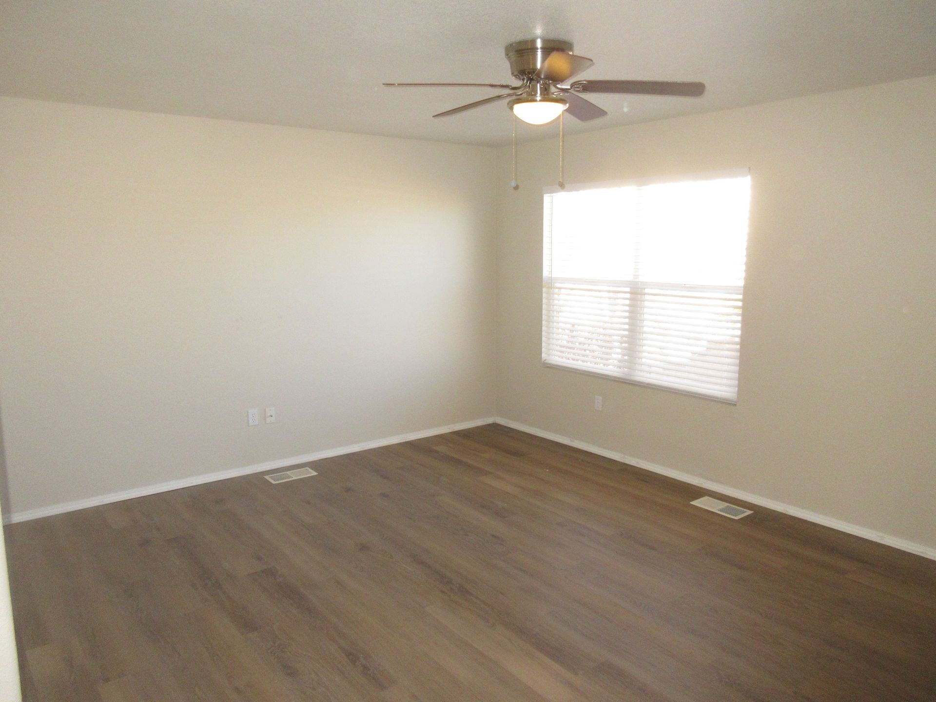 An empty room with hardwood floors and a ceiling fan.