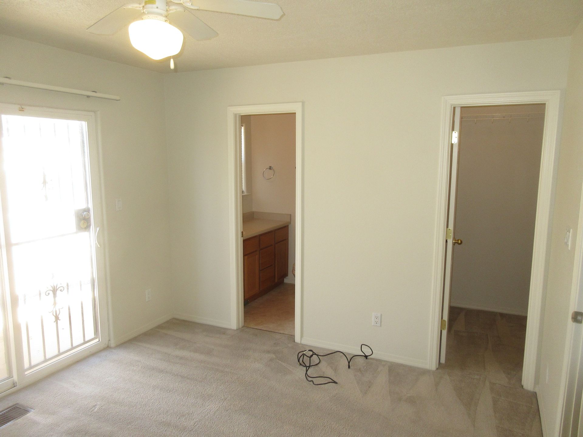 An empty room with a ceiling fan and a sliding glass door