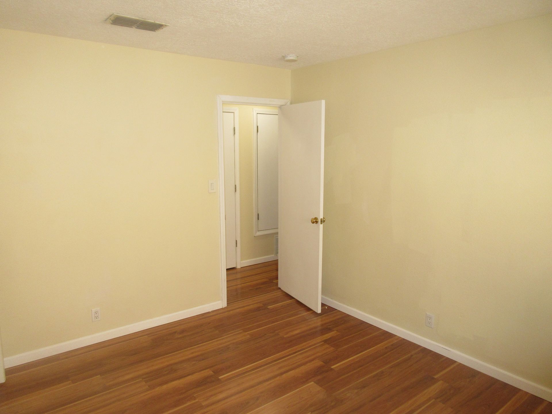 An empty bedroom with hardwood floors and a door leading to a bathroom.