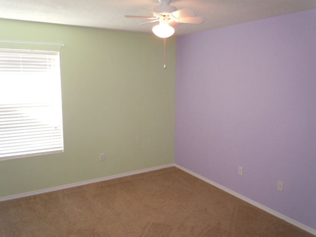 A bedroom with purple and green walls and a ceiling fan