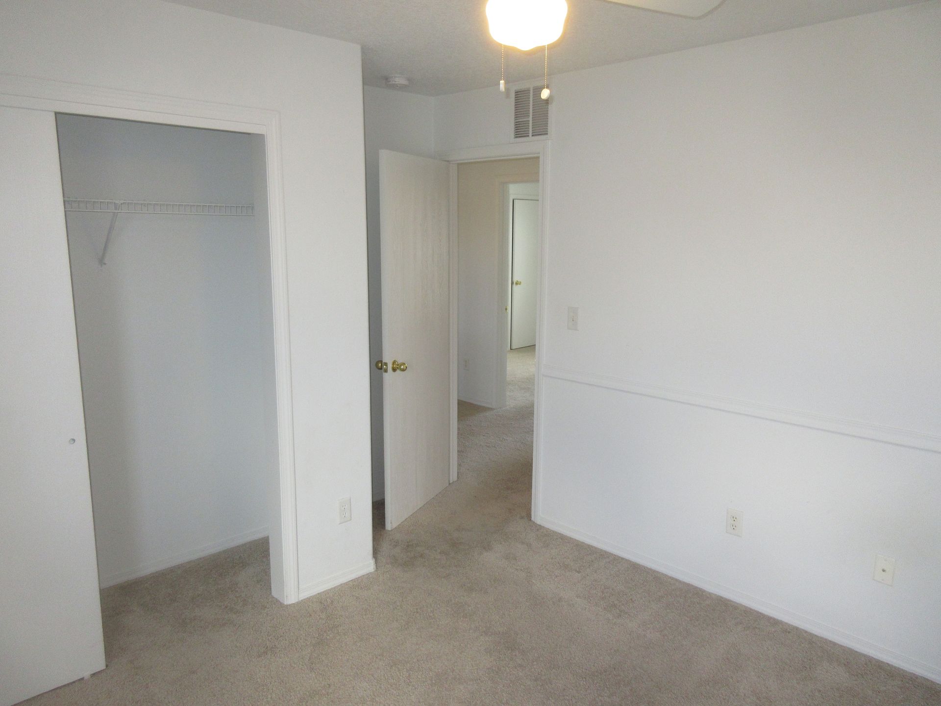 An empty bedroom with a ceiling fan and a closet.