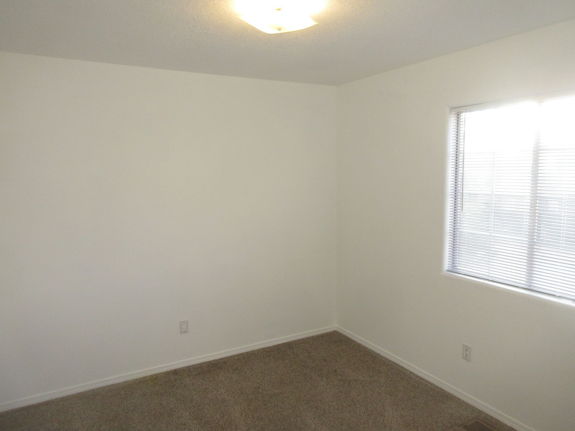 An empty bedroom with a window and blinds.