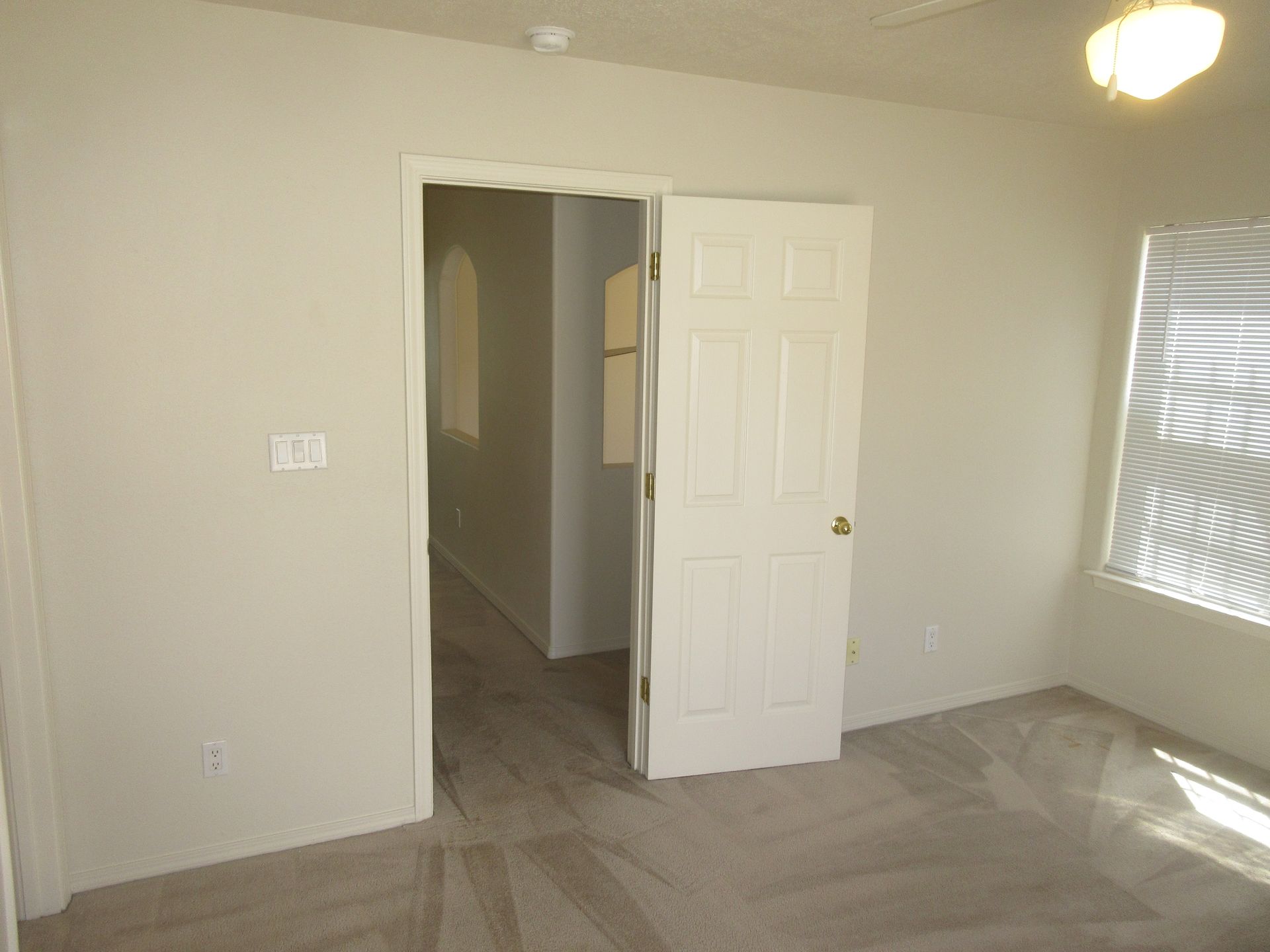 An empty bedroom with a door open and a window.